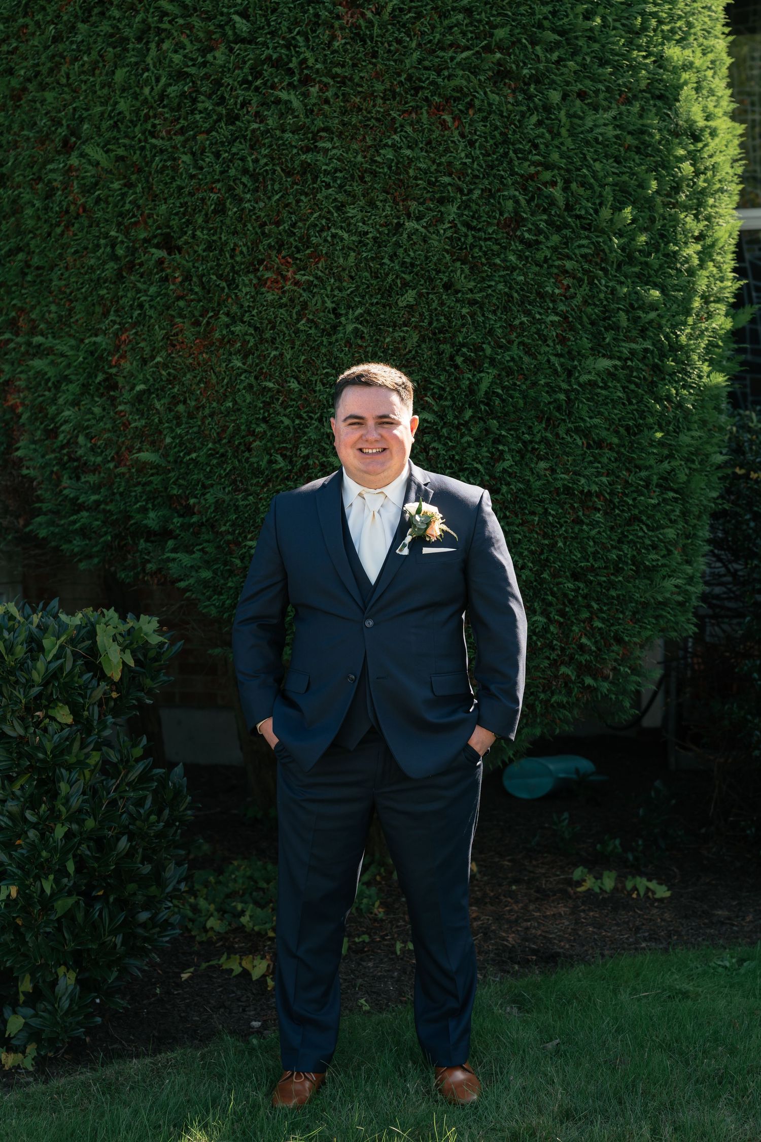 Wedding portrait against manicured green hedge background.