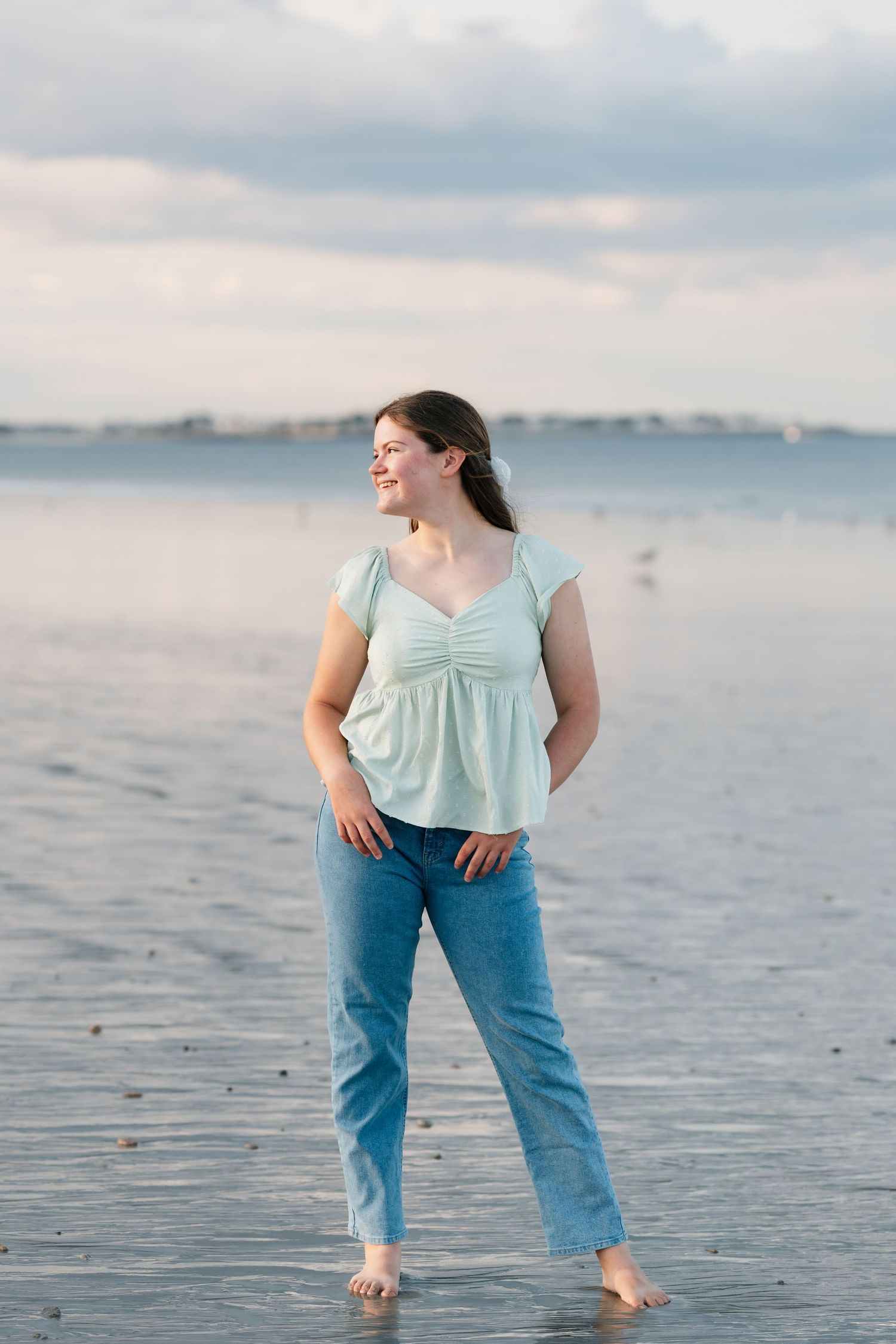 Casual beach portrait with seafoam green top and jeans against cloudy coastal sky.