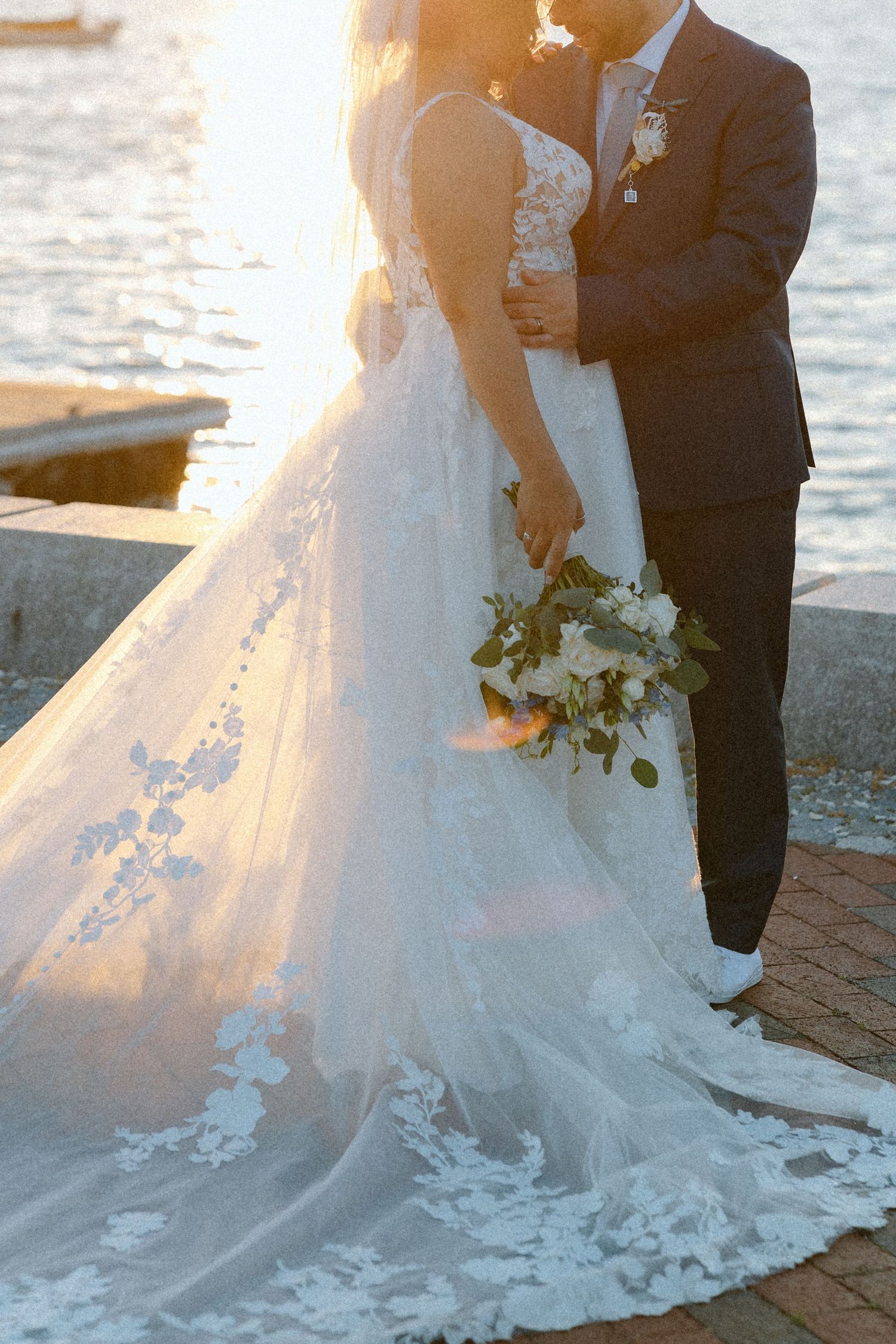 A sunset wedding photo showing the intricate lace details of a bride's trailing gown.