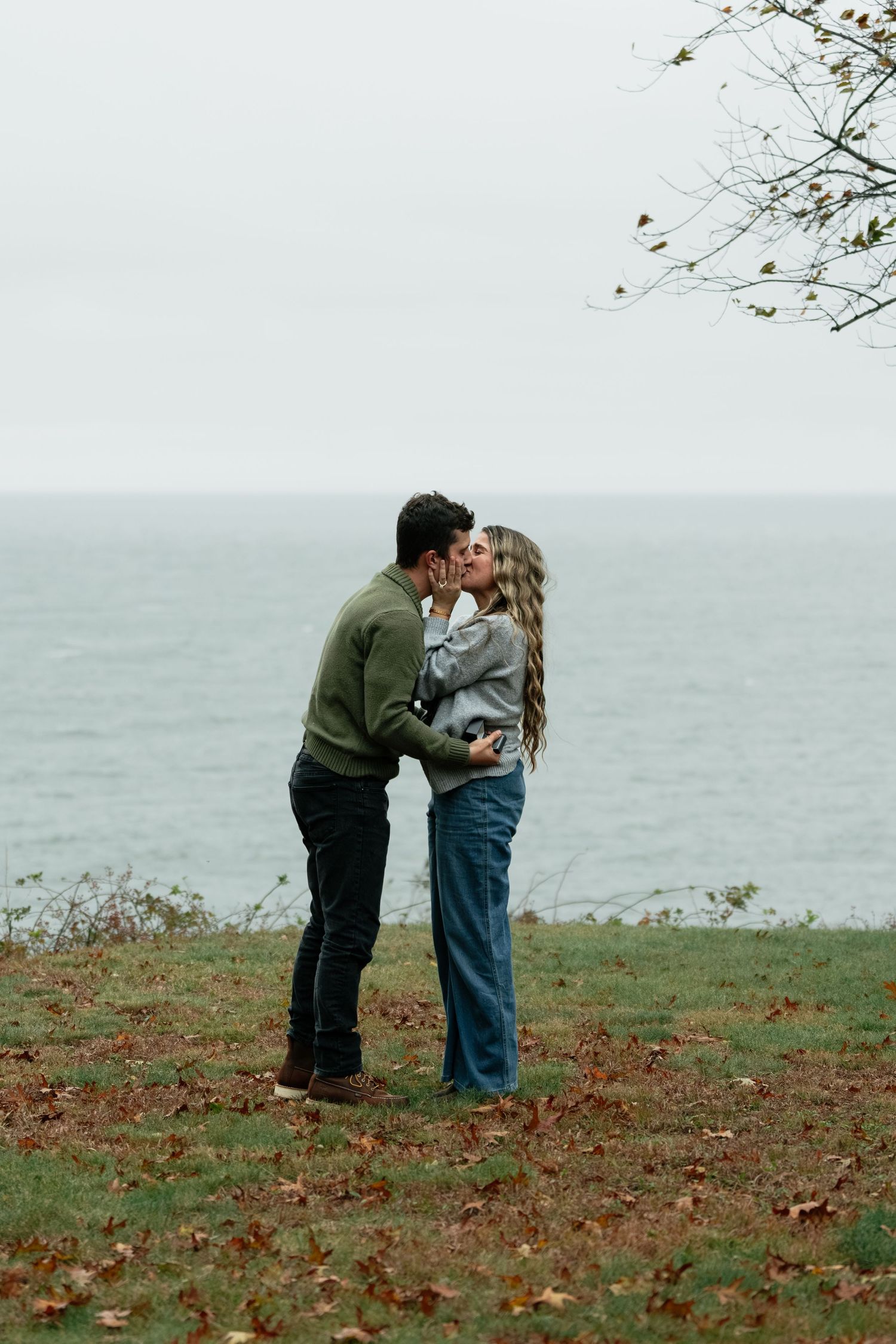 Two people share a romantic moment on a hillside covered in fallen leaves by the sea.