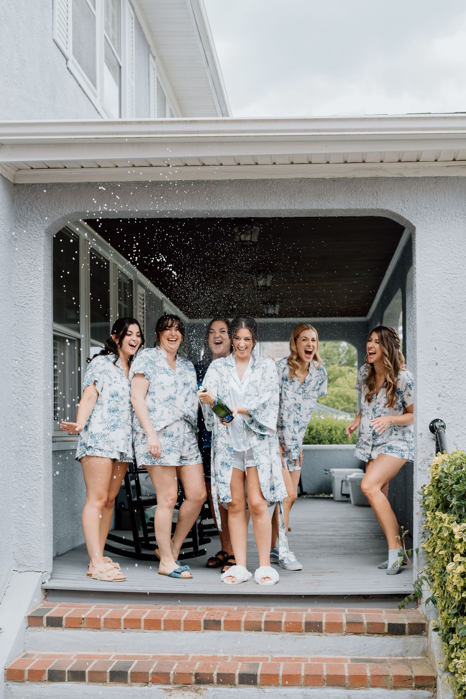 Wedding party in matching floral robes celebrating on a porch.