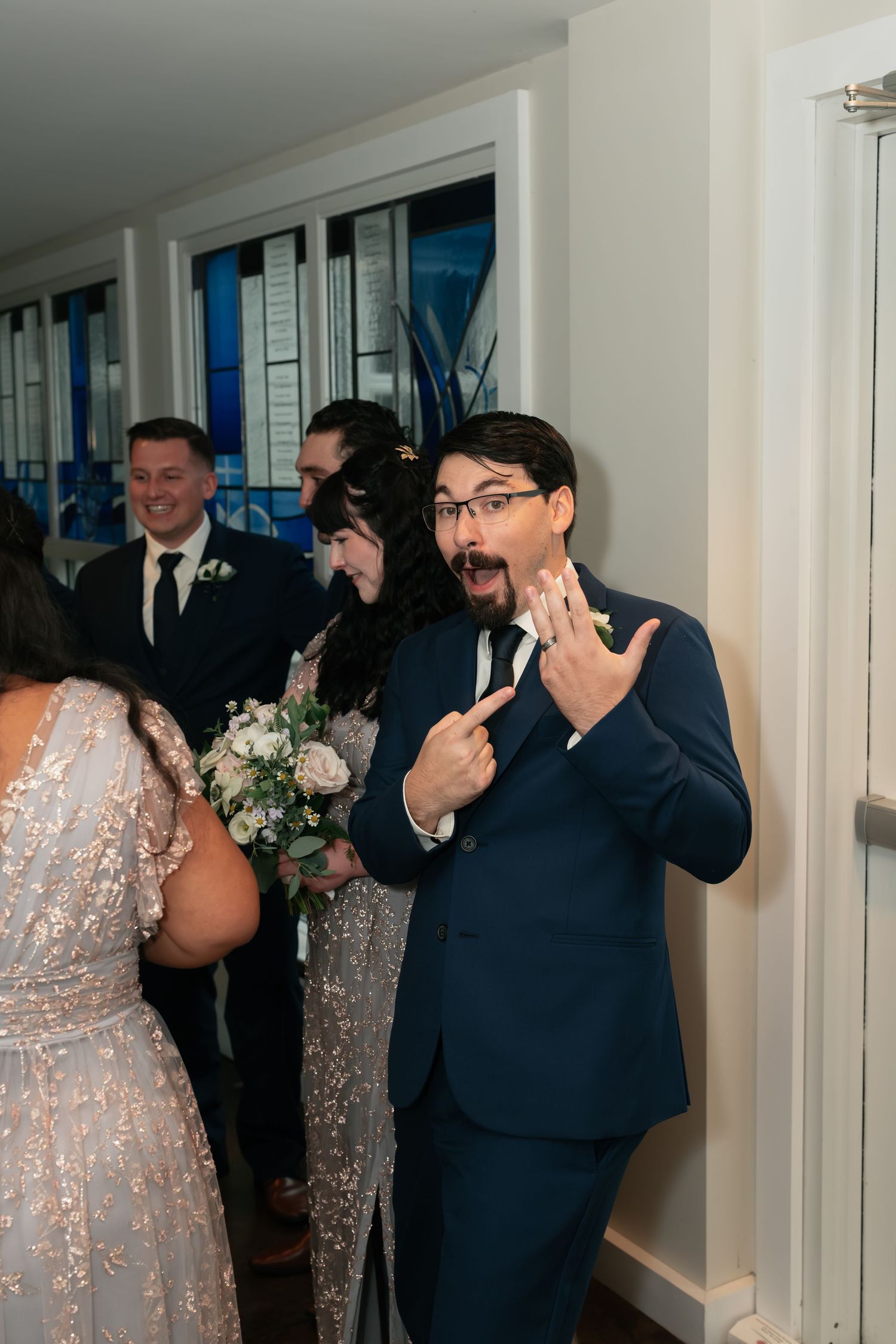 Wedding celebration in a bright hallway with formal attire and floral decorations.