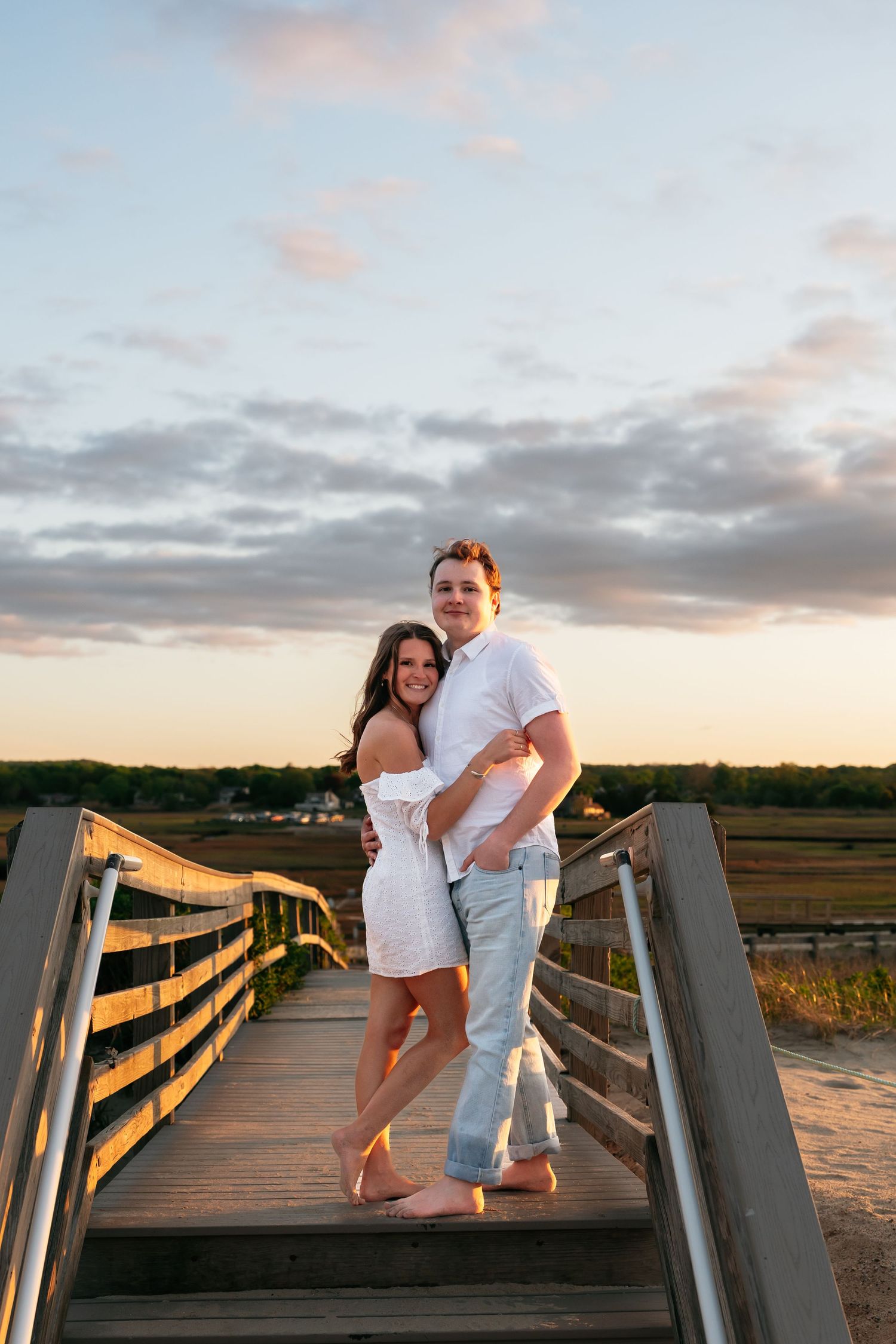 A couple posing playfully on a wooden boardwalk at golden hour.