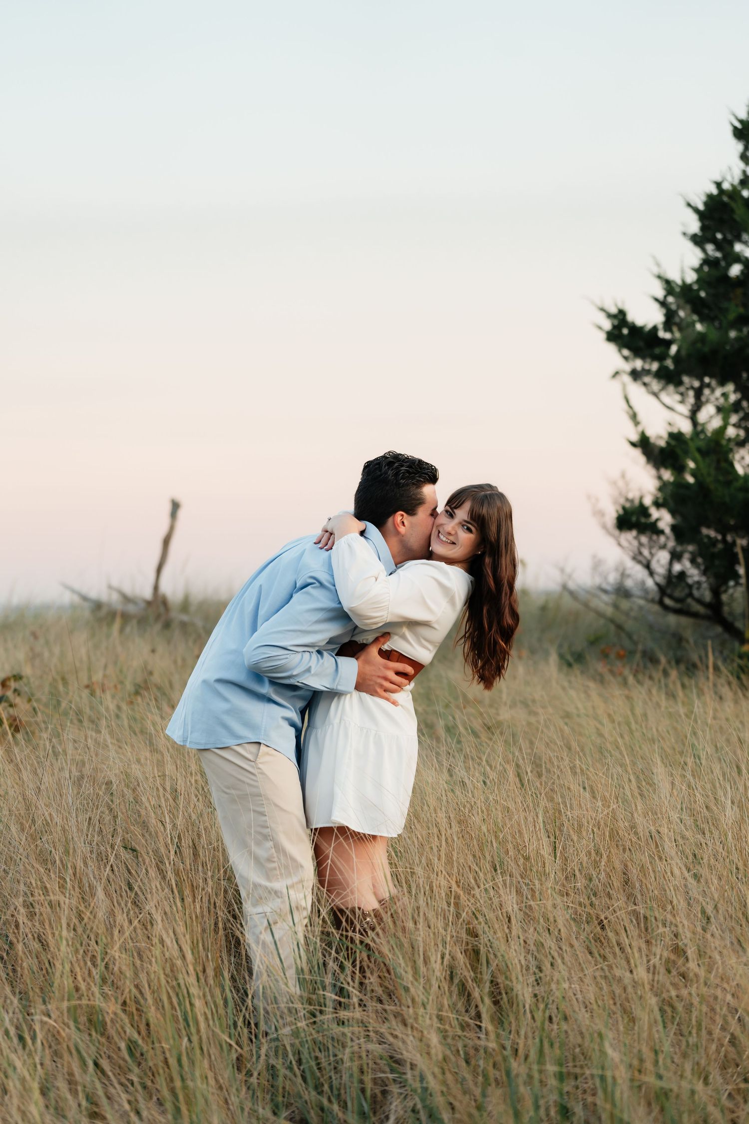 A couple embraces in a field of tall grass during sunset.