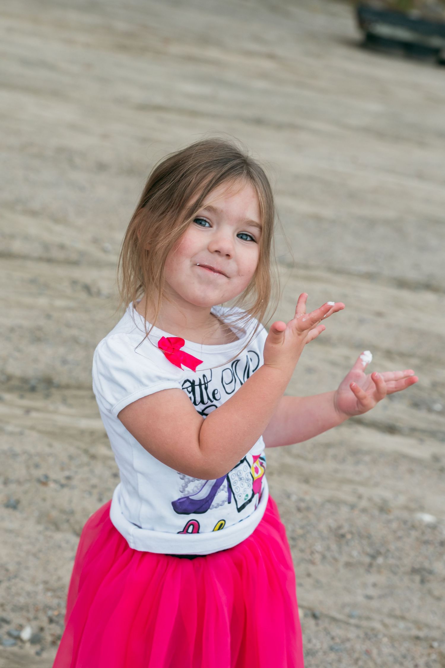 A cheerful pose is struck while wearing a vibrant pink tutu and graphic t-shirt on the beach.