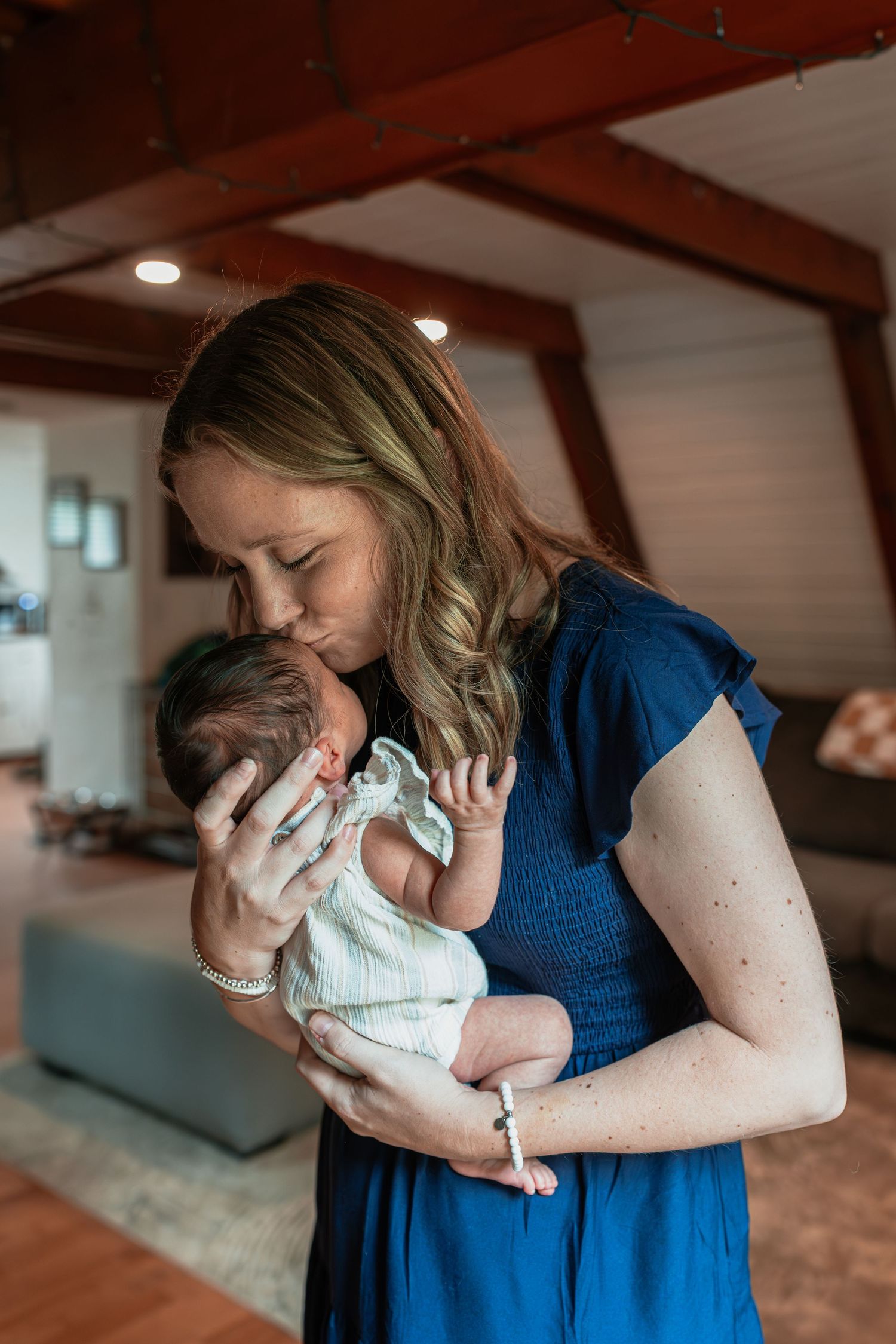 Mother in blue dress tenderly holding and bonding with newborn baby indoors.