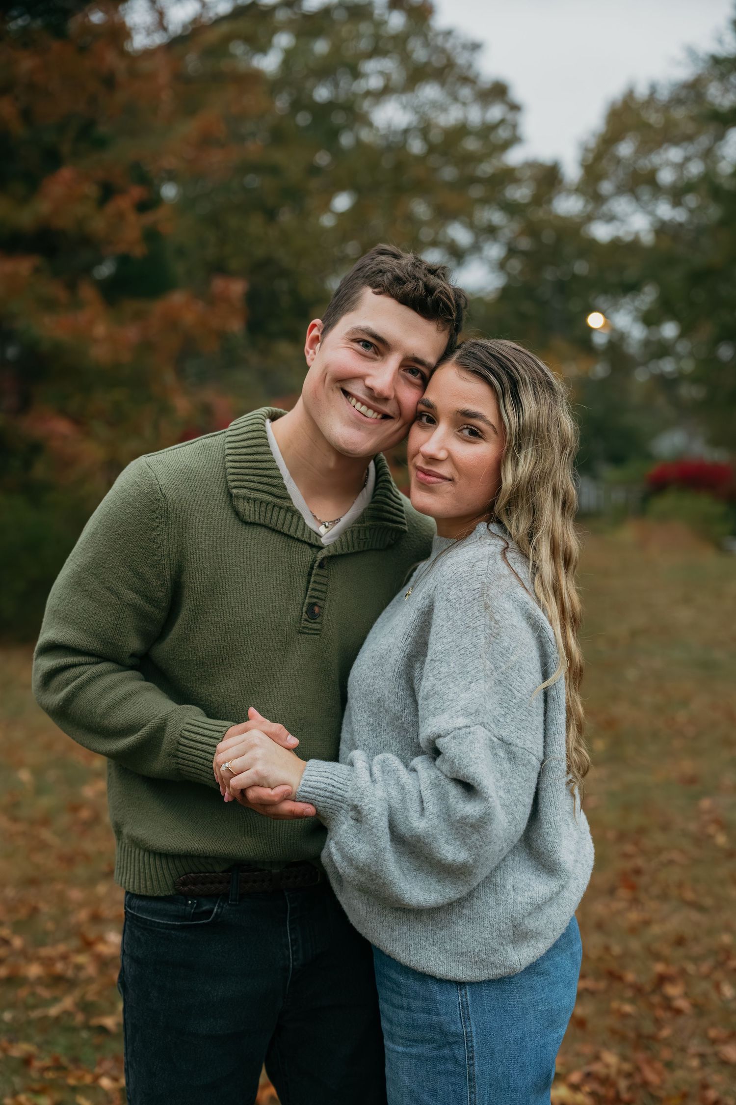 Two people in casual sweaters share an intimate moment outdoors in autumn.