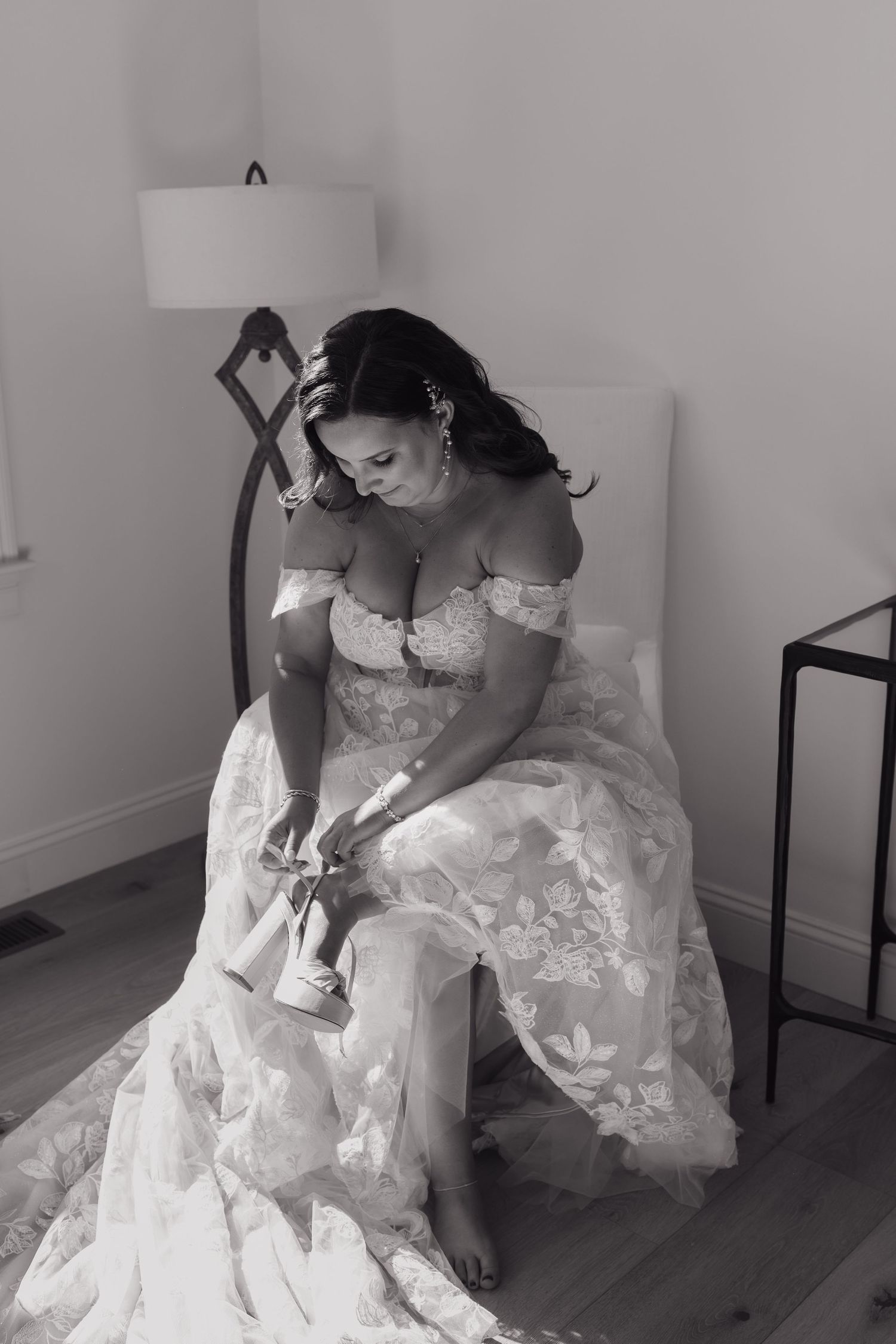 Bride adjusting her shoes while seated in an elegant lace wedding gown.