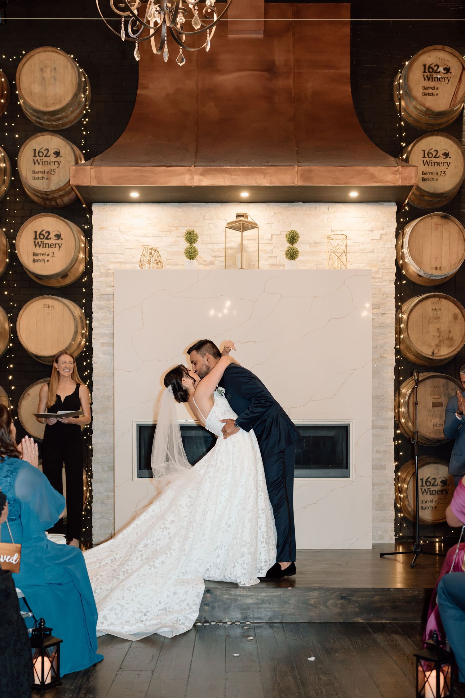 Wedding couple dances in rustic winery venue with barrel decor and string lights.