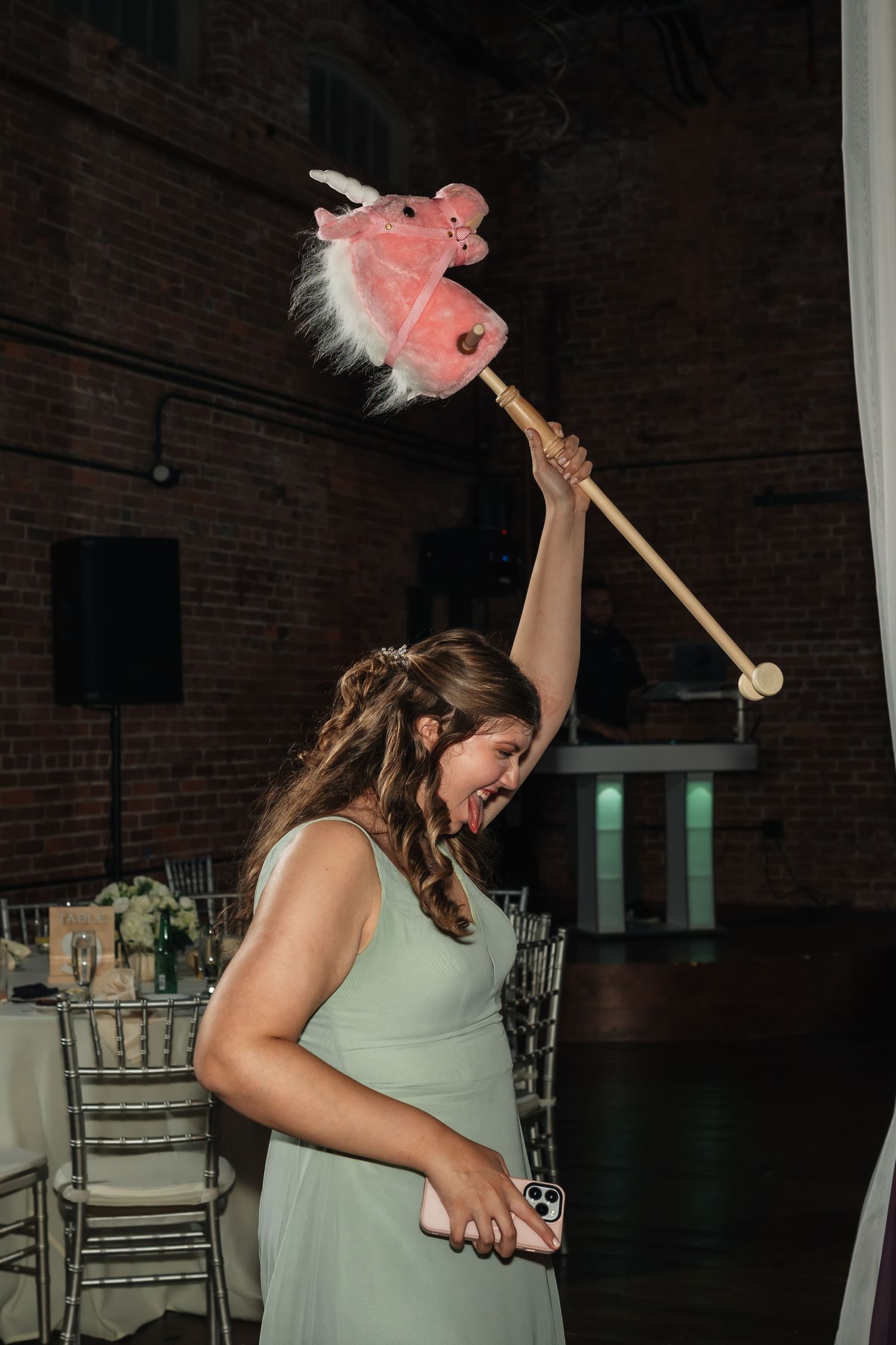 Bridesmaid in mint green dress dancing with pink prop at wedding reception.