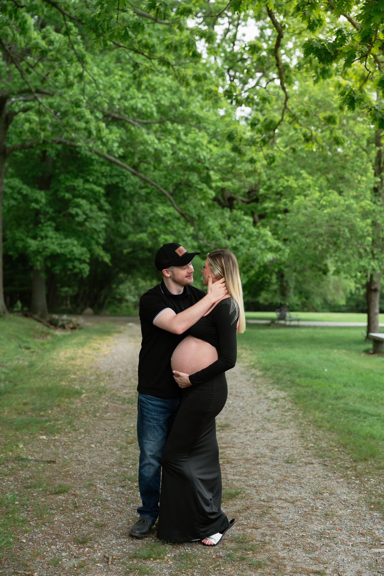 Couple embracing during maternity photoshoot on wooded path.