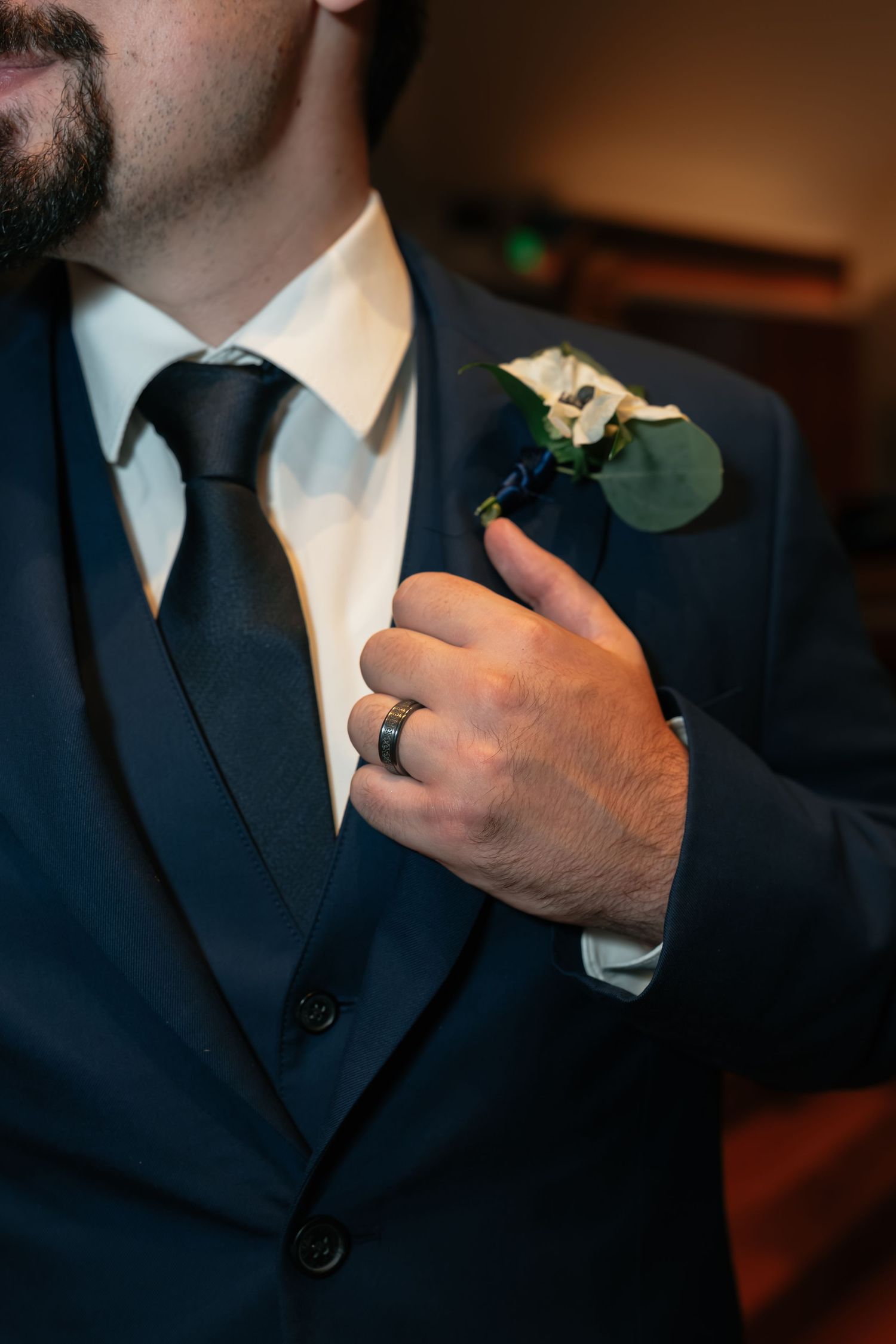 Close-up of groom's boutonniere and wedding ring against navy suit.