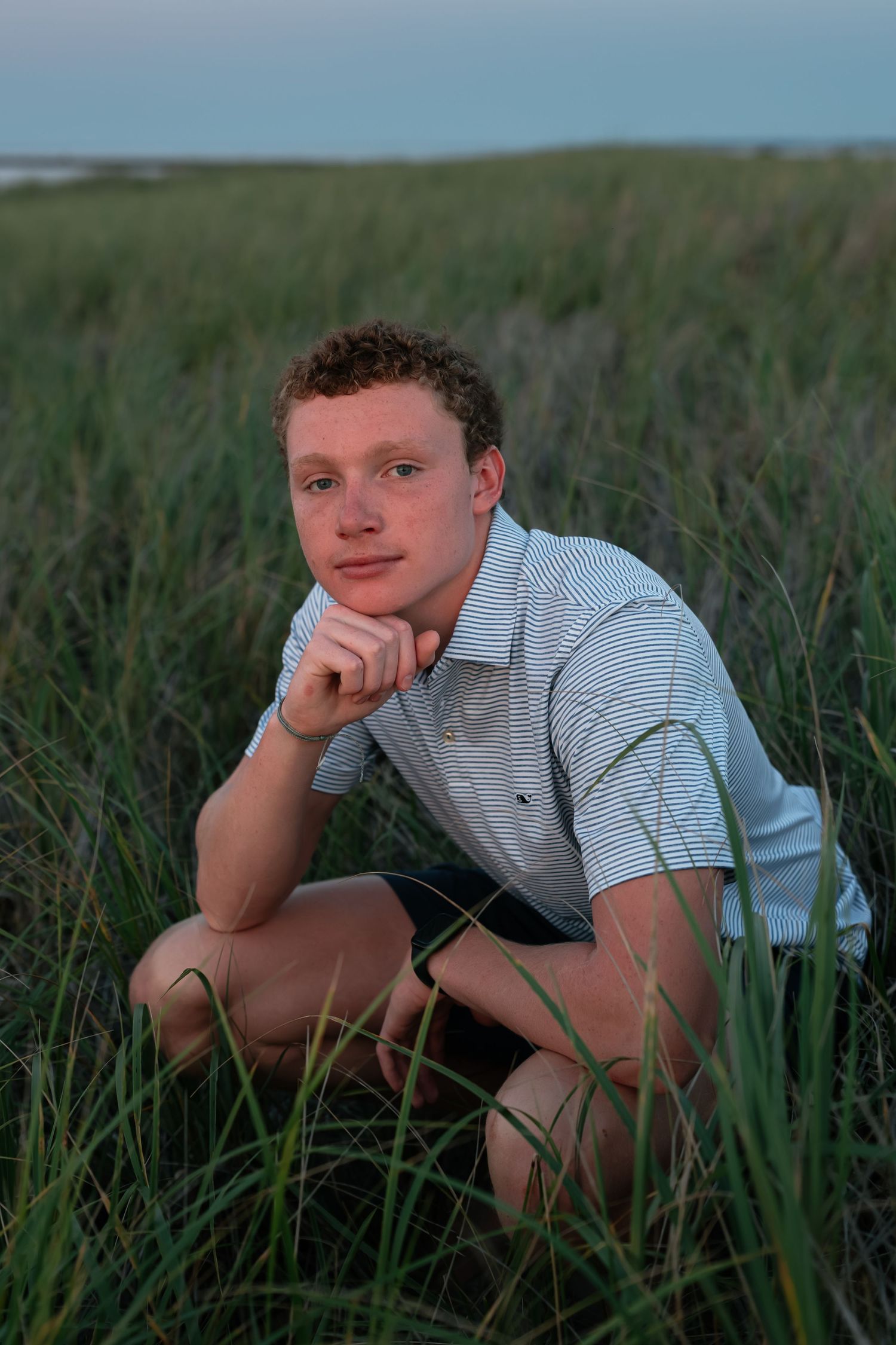 Person in striped polo shirt reclines in green grass during outdoor photo session.