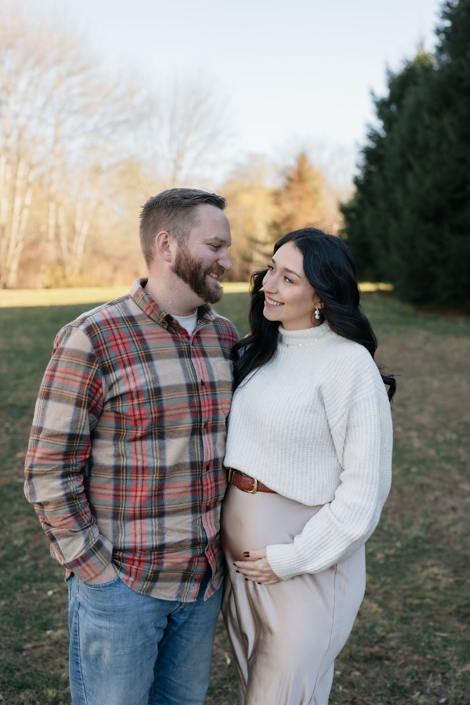 Couple in casual winter attire share intimate moments in an outdoor photoshoot against evergreen trees.