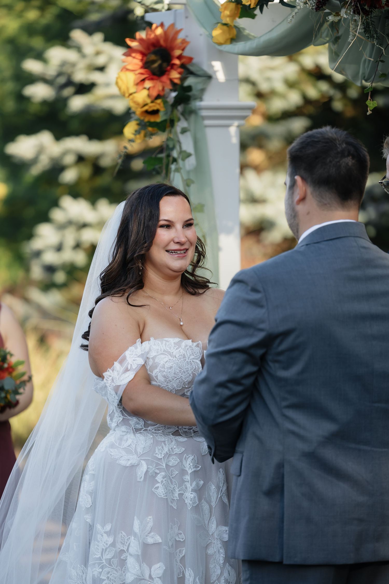 A couple shares a joyful moment during their wedding ceremony under a floral-decorated arbor.