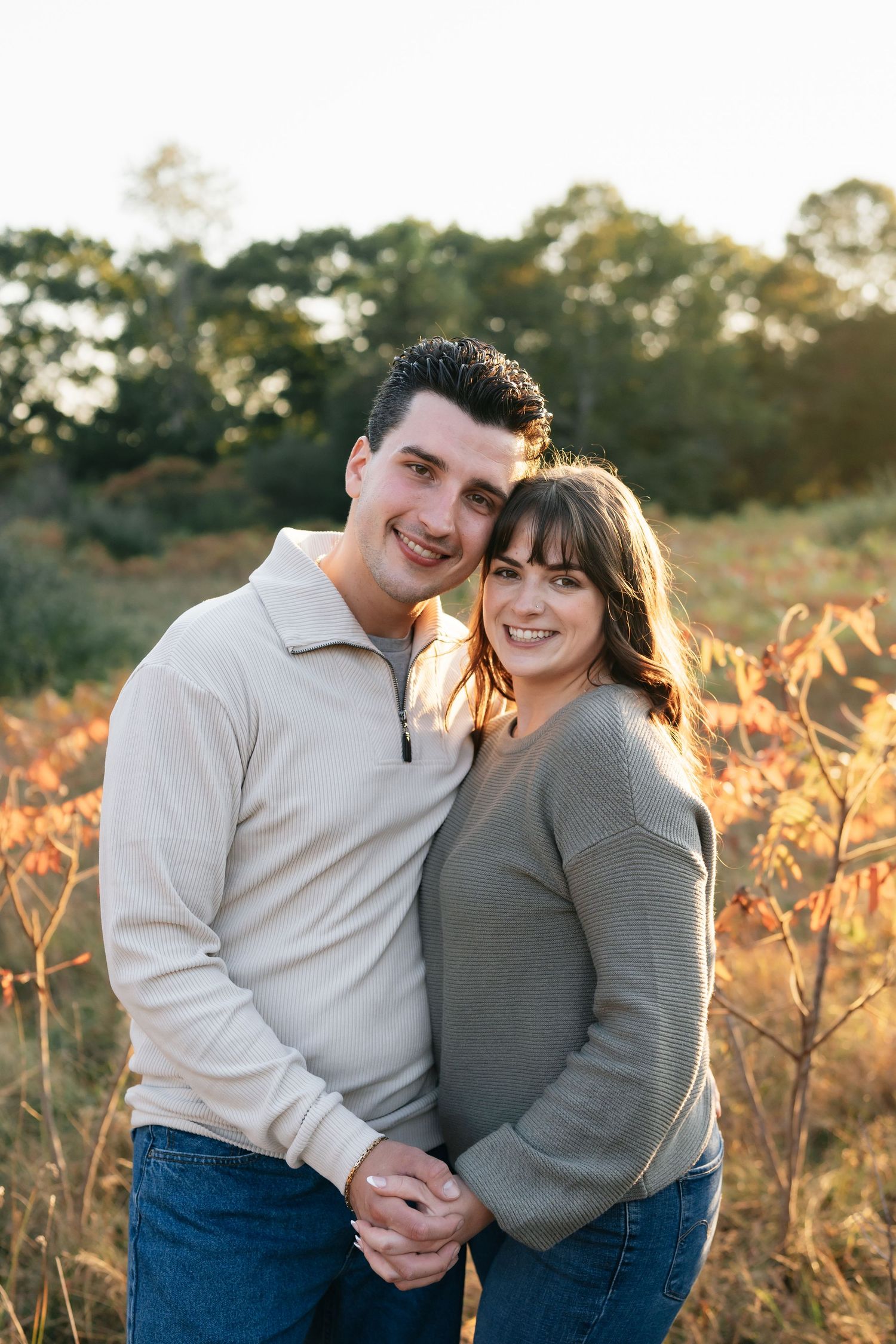 A couple laughs together in a sun-drenched field during golden hour.