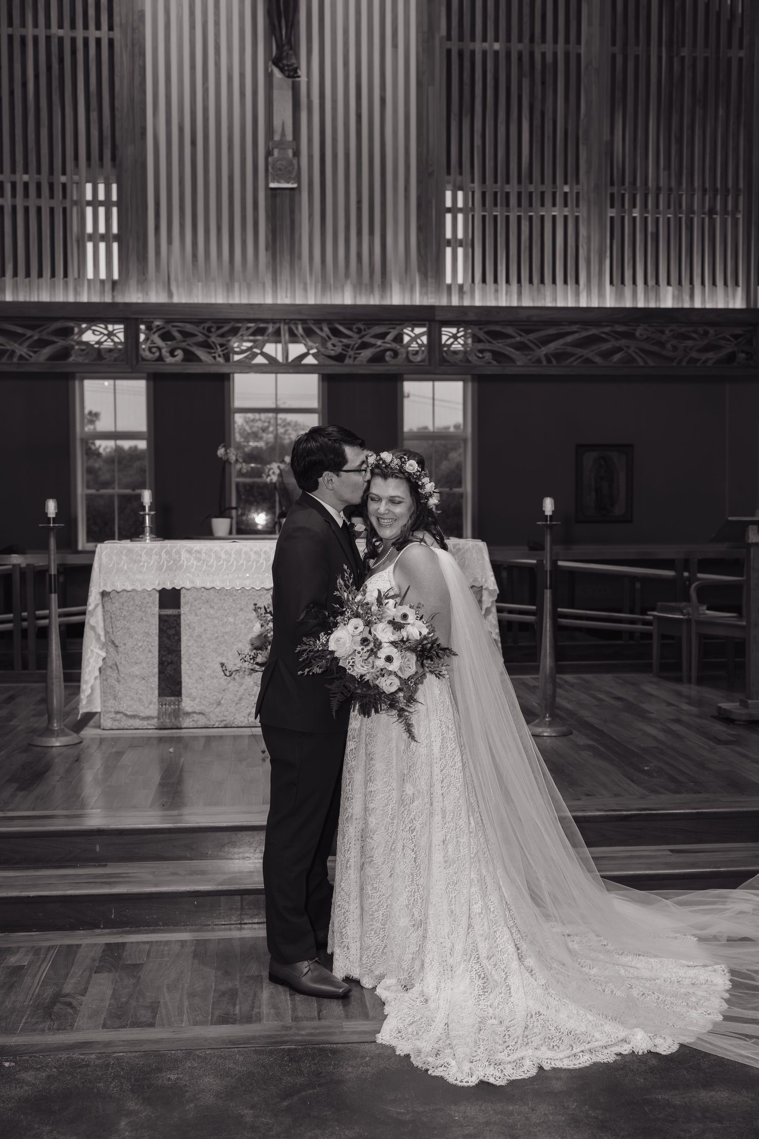 A black and white photo captures a tender moment between newlyweds in a church setting.