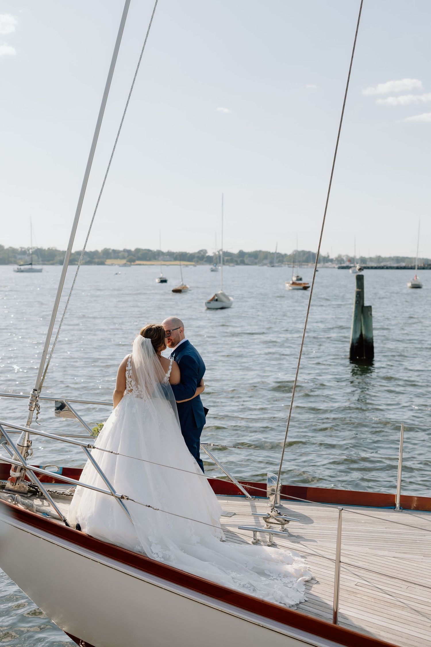A wedding couple embraces on the deck of a sailboat with harbor views.