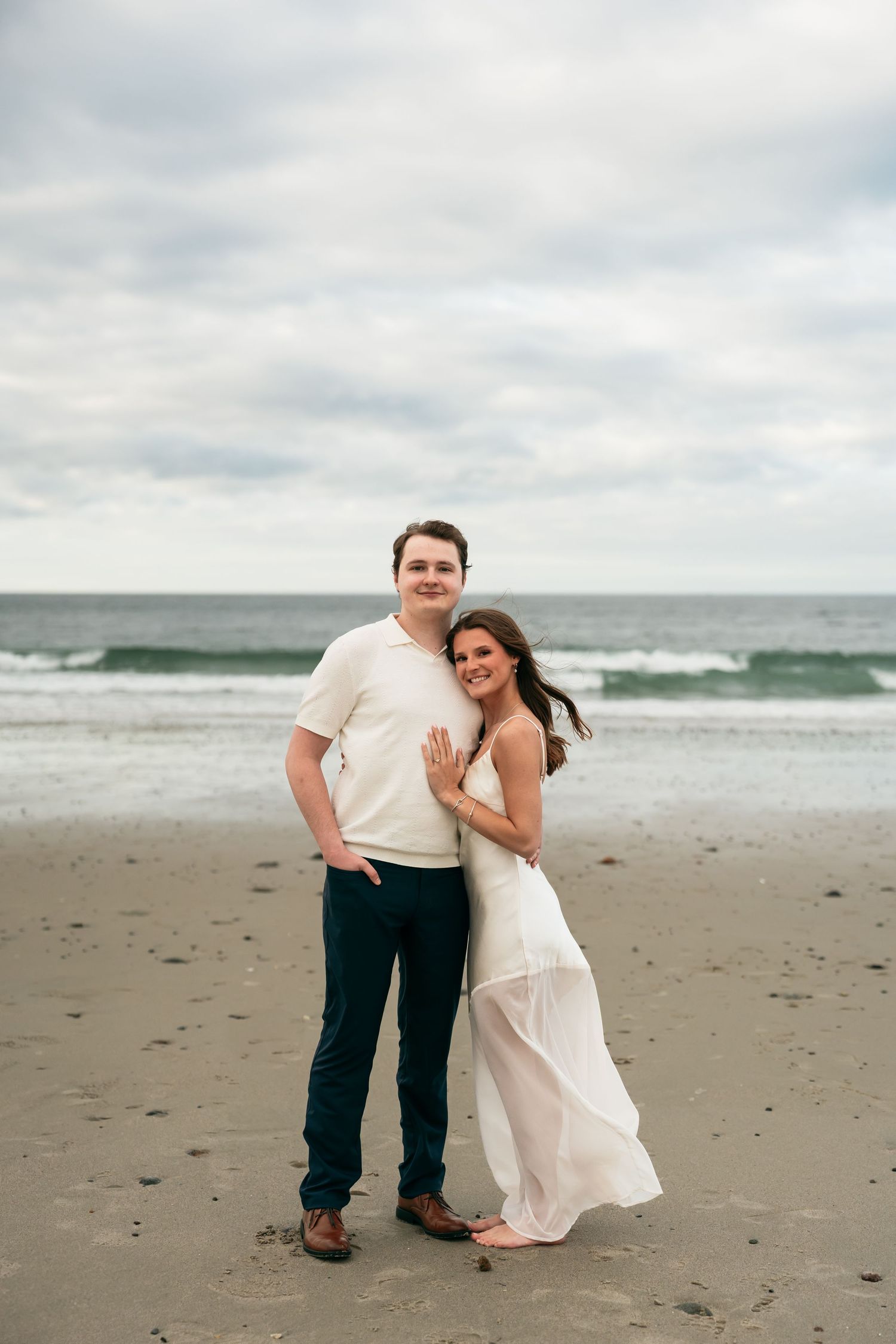 A couple shares a tender moment together on a cloudy beach.