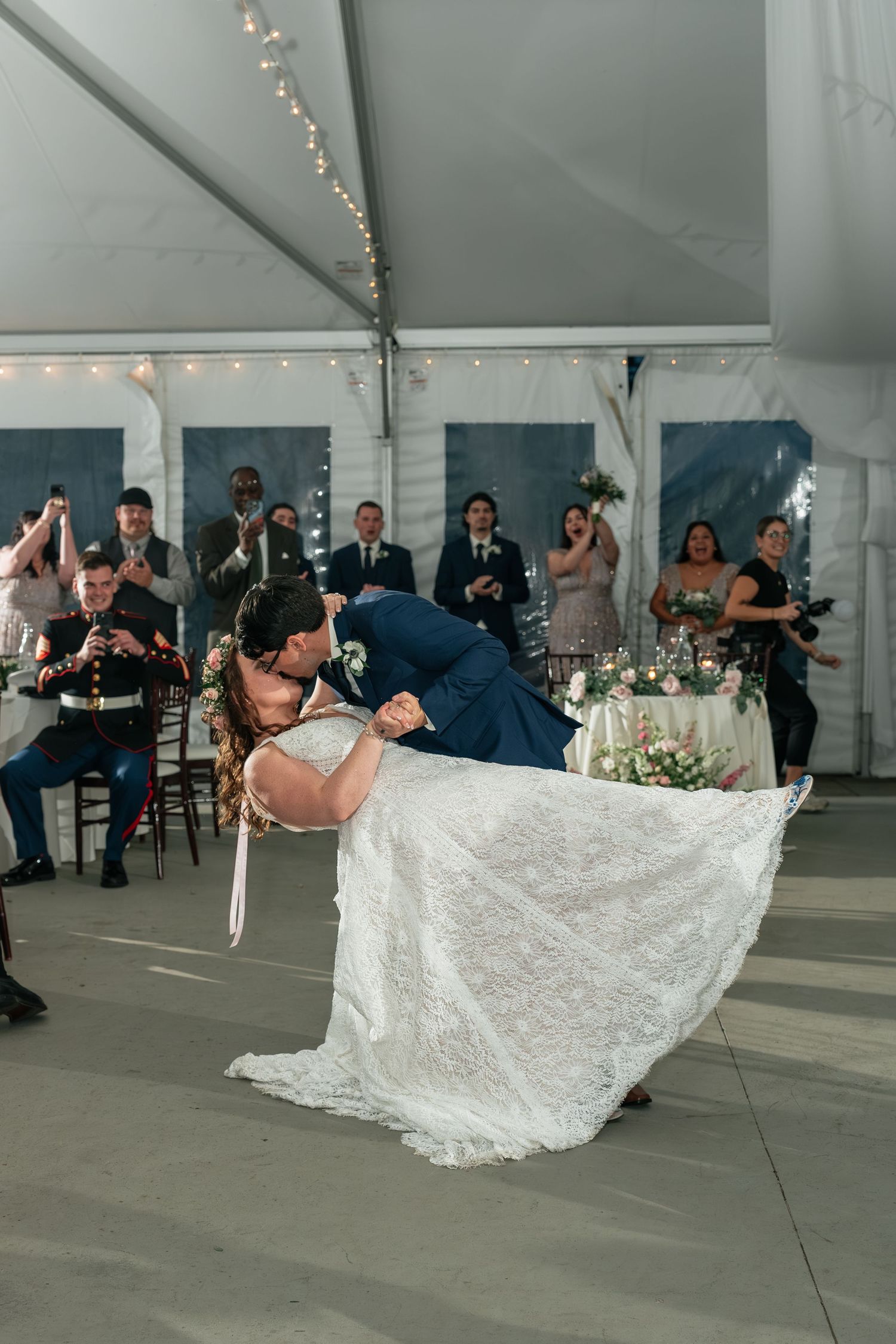 Couple performs romantic dip during first dance at wedding reception under string lights.