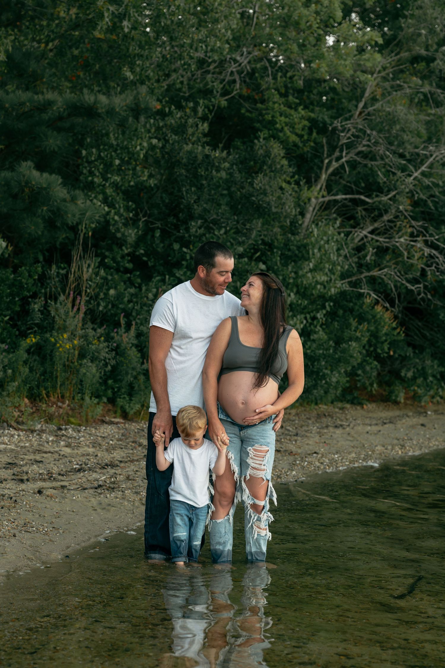 Family wading in lake water together during sunset maternity photo session.