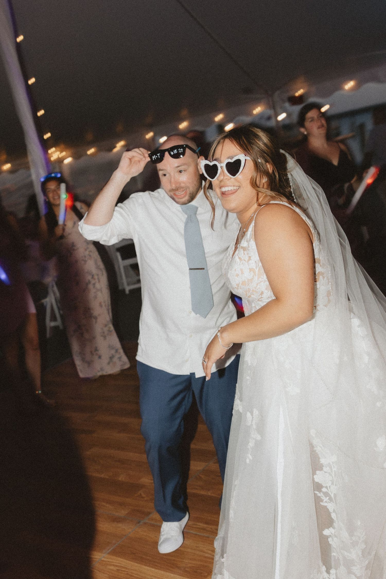 Wedding reception dance party with guests and bride in white dress dancing under string lights.