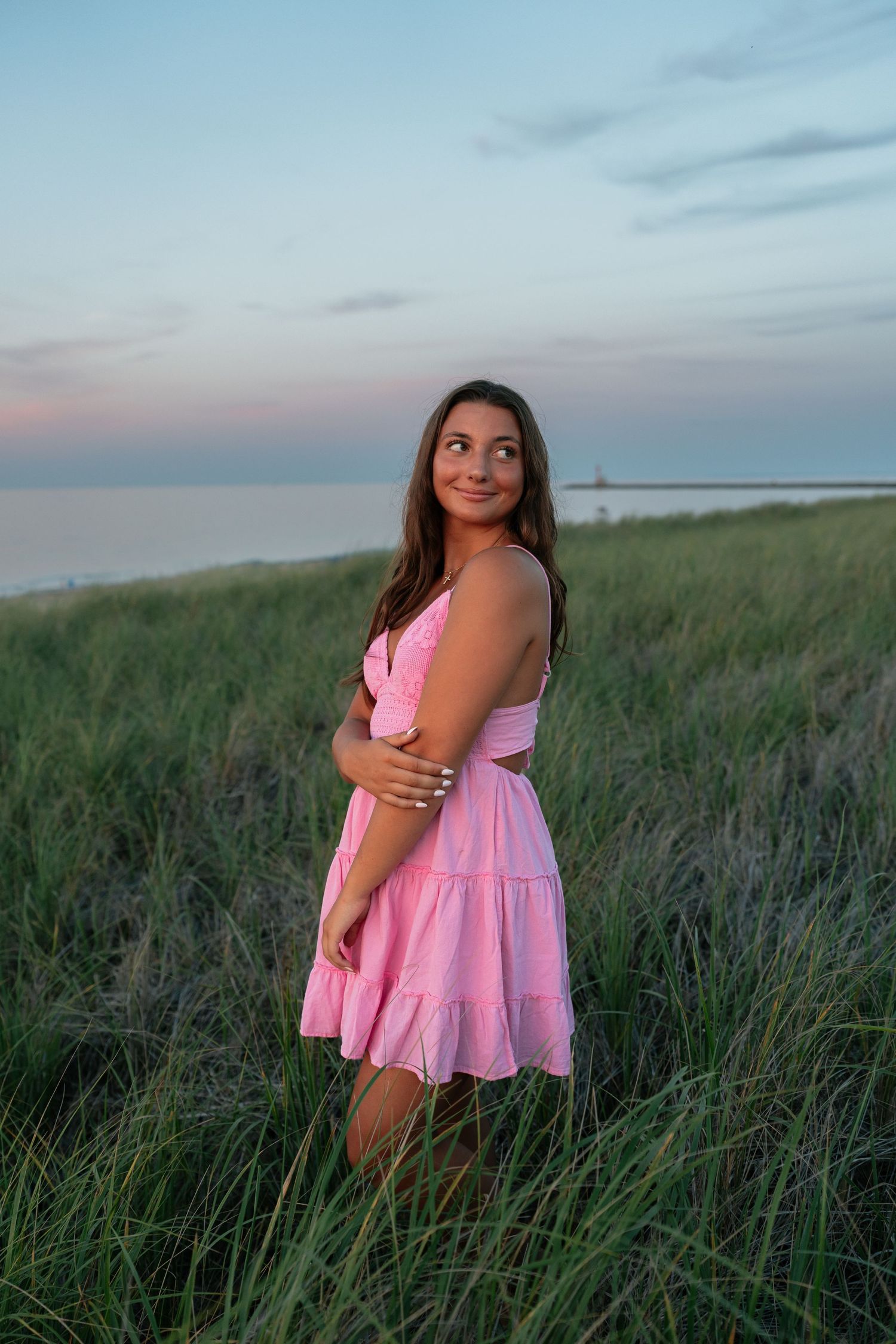 Pink dress contrasts with tall beach grass during coastal photoshoot.