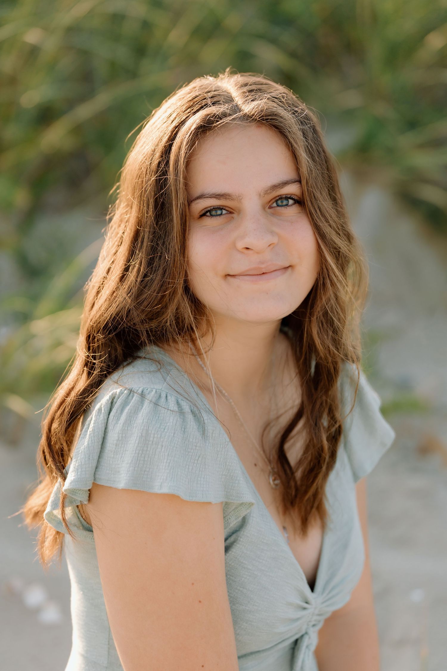 Natural light portrait in sage green top against beach grass background.