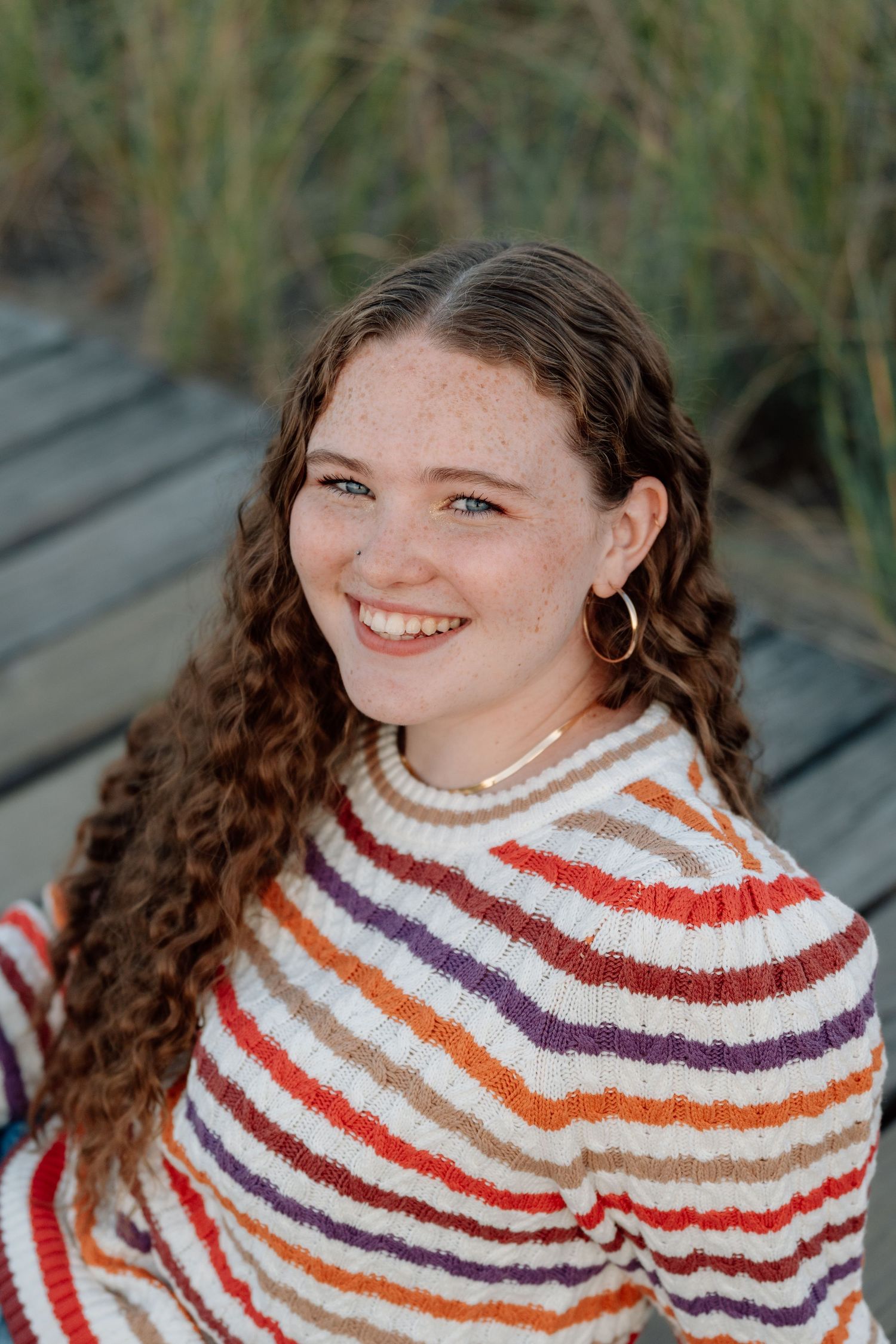 Person wearing a colorful striped sweater sitting outdoors.
