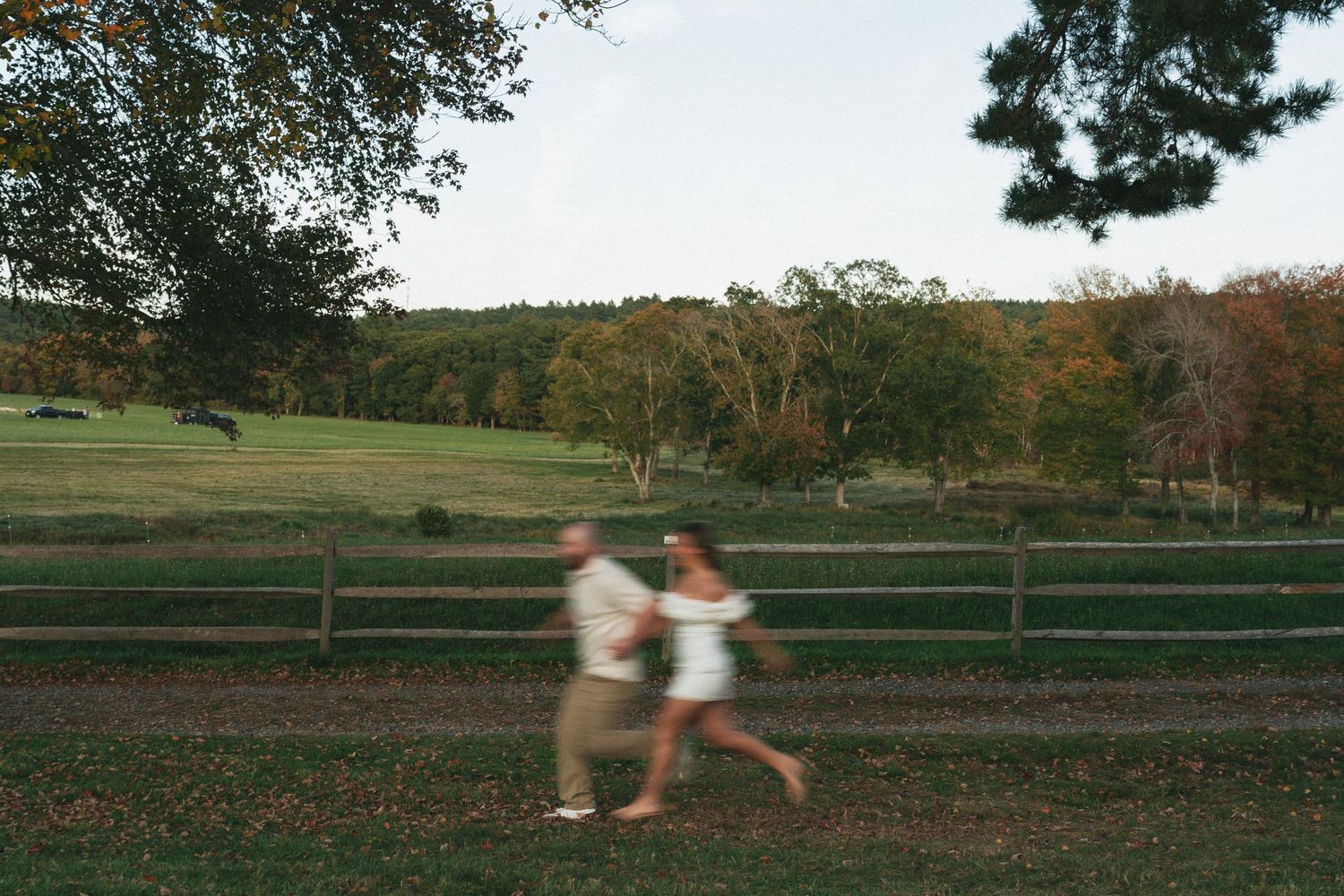 Motion blur captures couple running along rural fence line at dusk.