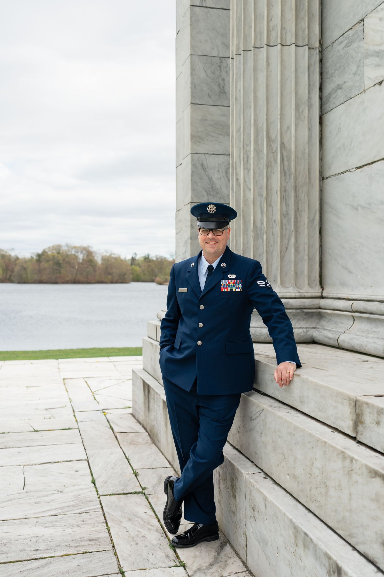 Military service member in dress blues posing against classical stone columns.