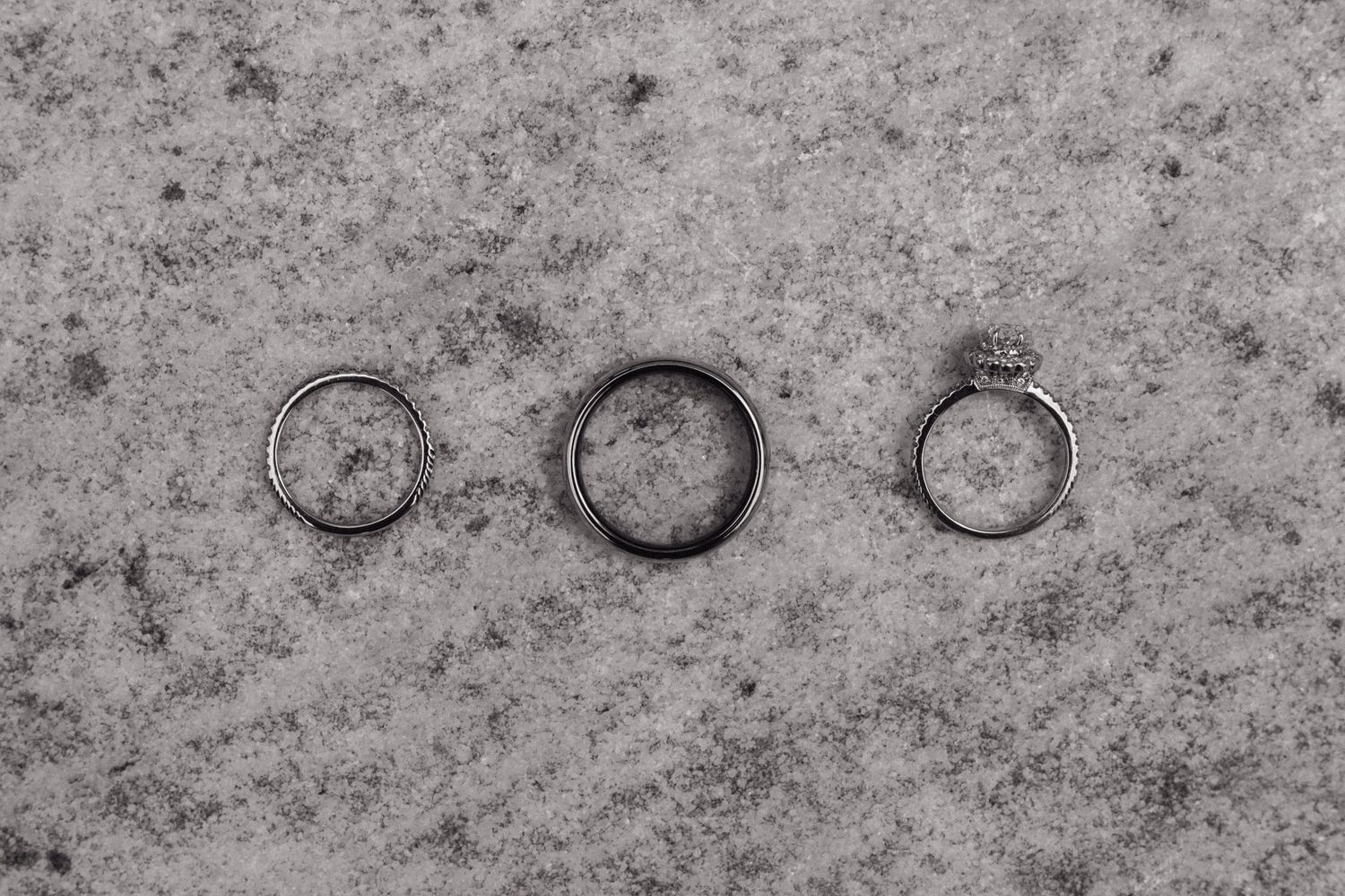 Three wedding rings arranged in a row on a textured gray surface.