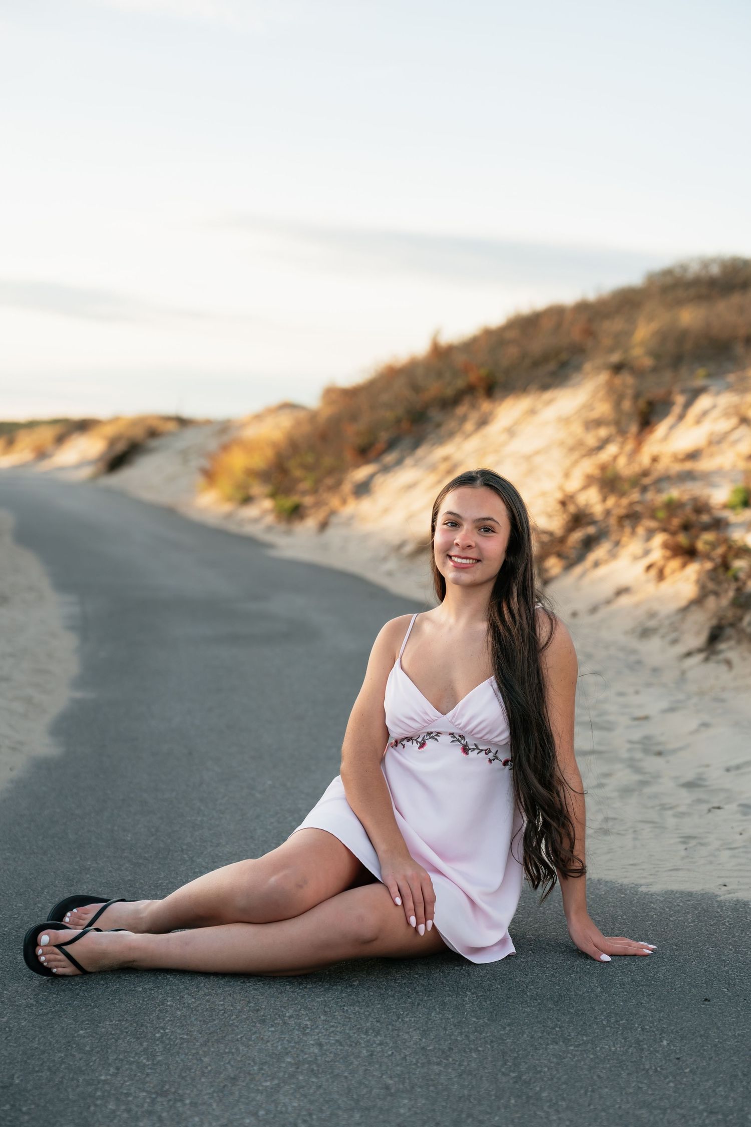 Person in white top reclining on dark pavement near beach dunes.