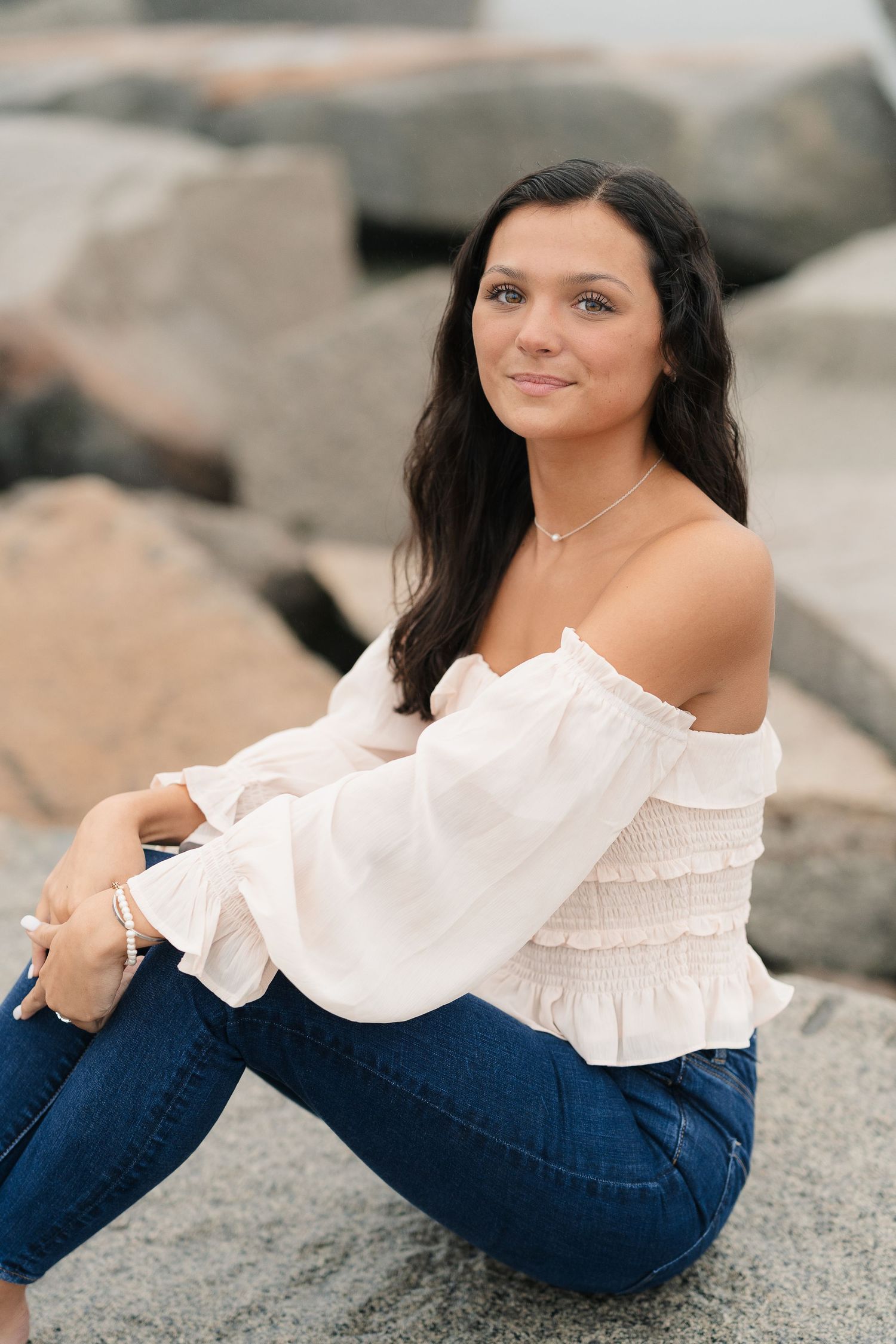 Casual portrait on rocky beach wearing white top and jeans.