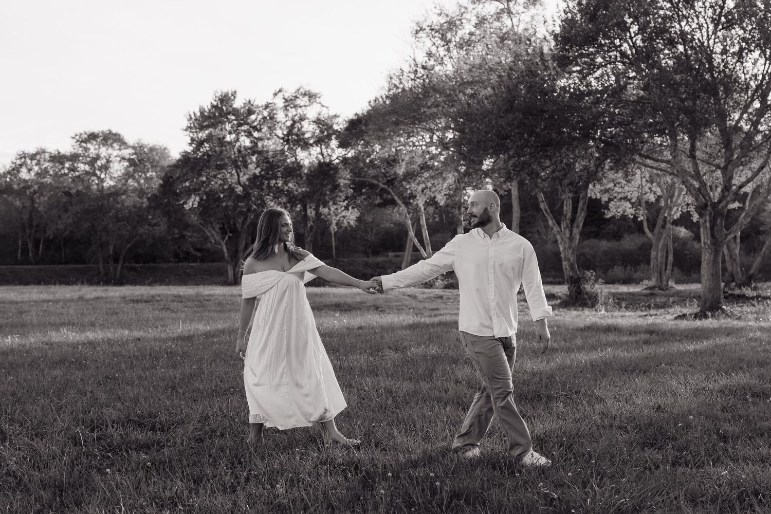 Black and white photo of a couple dancing in a field with trees in the background.