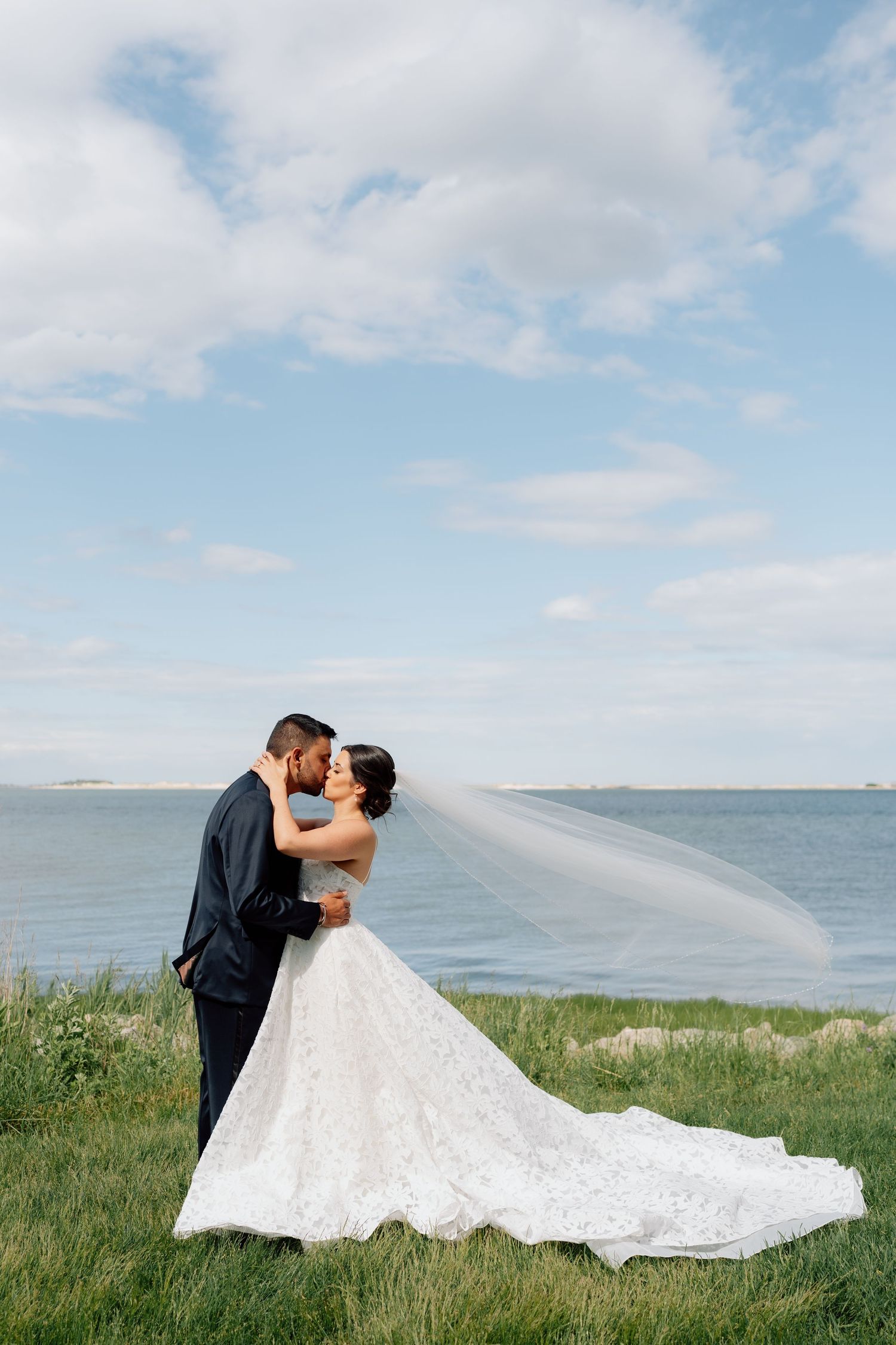 Wedding couple poses in front of scenic coastal landscape with flowing white dress.