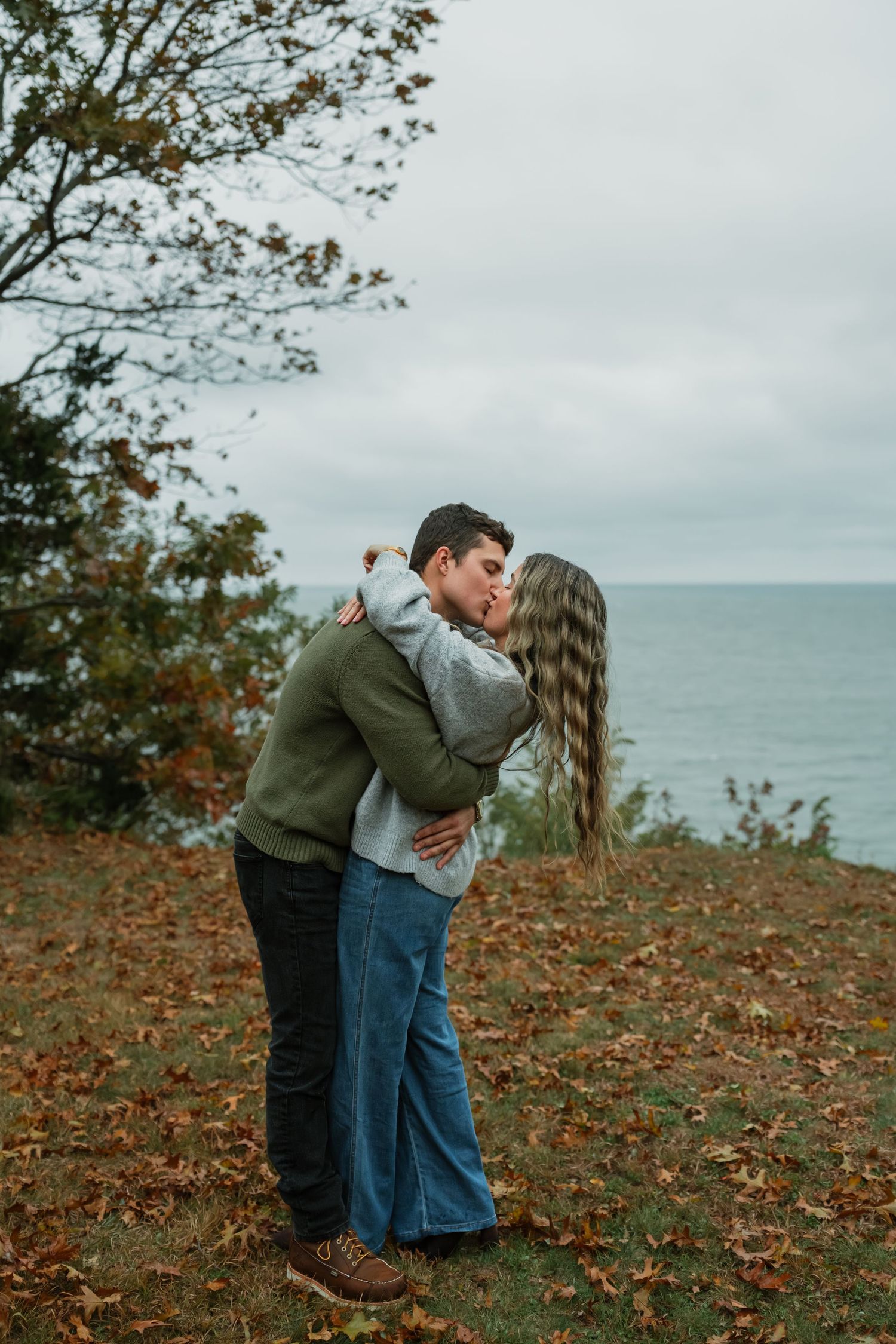 A couple shares a romantic kiss on an autumn hillside overlooking the ocean.
