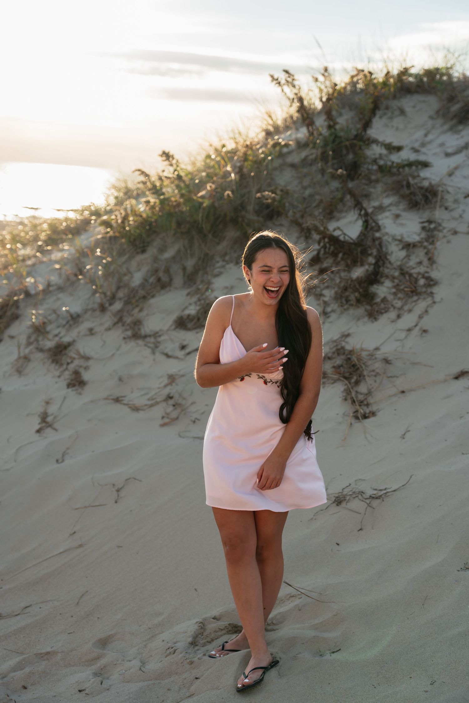 Person laughing joyfully while posing on sandy beach dunes at sunset.