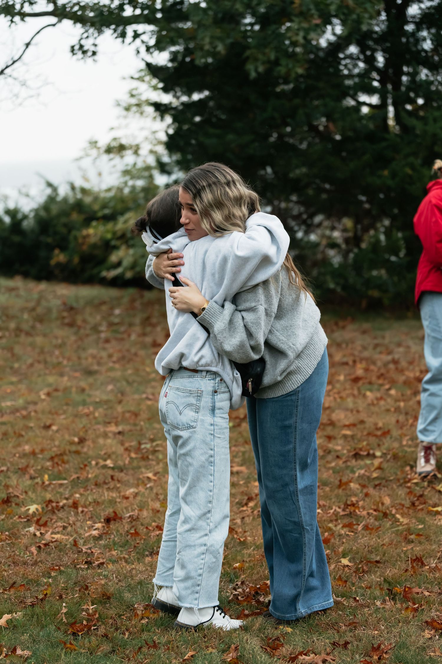 A couple embraces in a romantic moment on an autumn day with fallen leaves scattered on the ground.