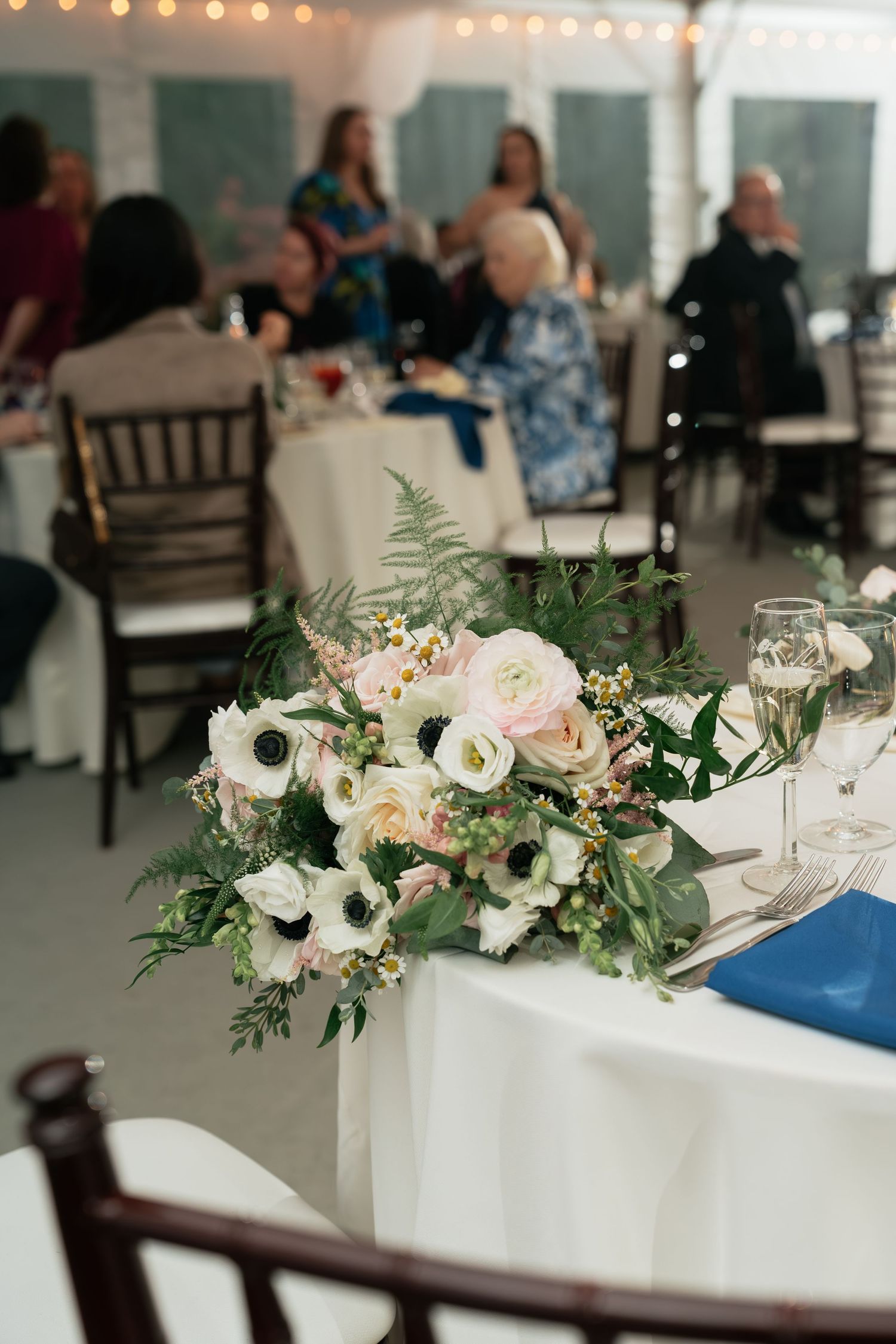 Wedding reception centerpiece featuring white and pink flowers with greenery on white tablecloth.