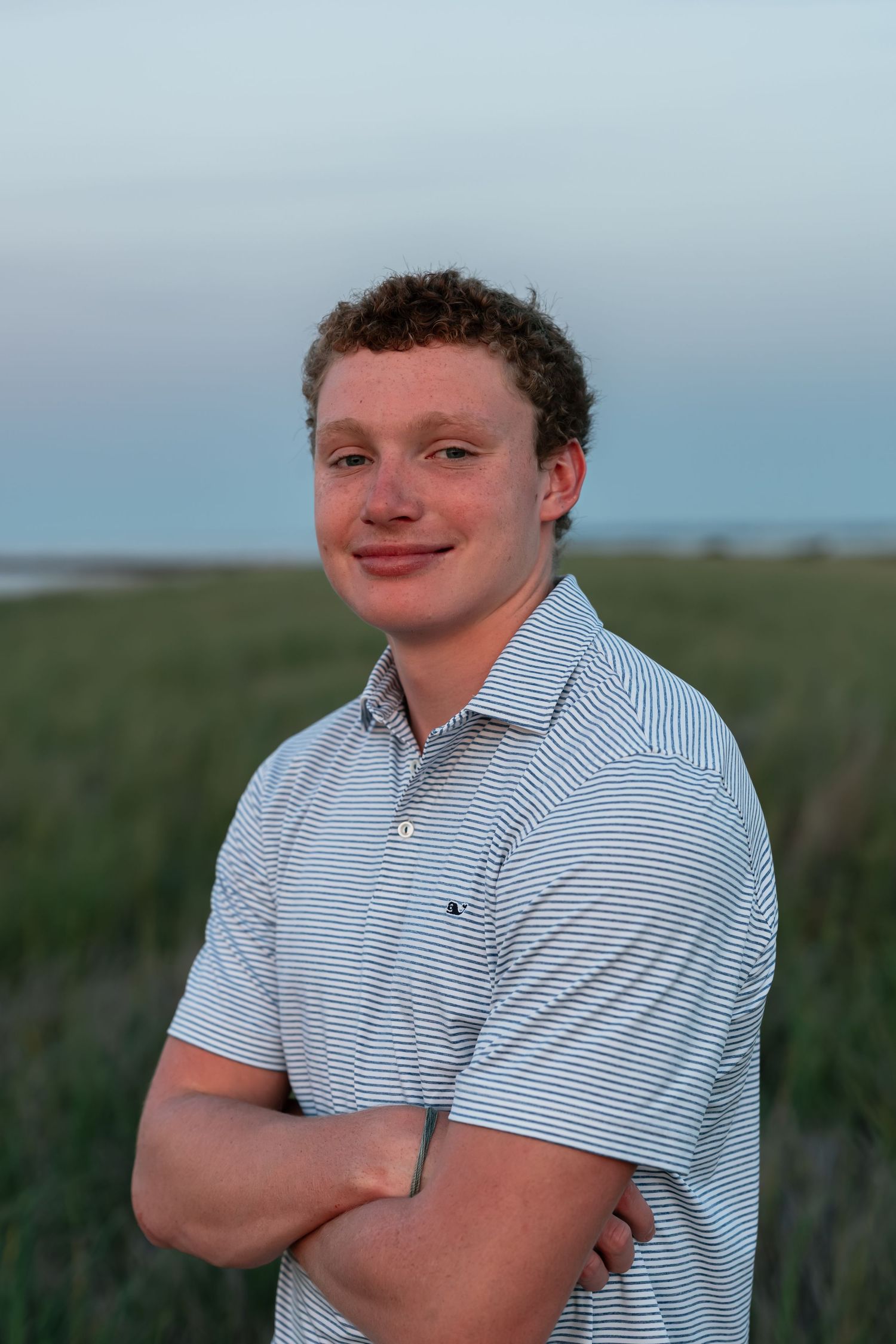 A person in a striped polo shirt poses outdoors against a natural background.