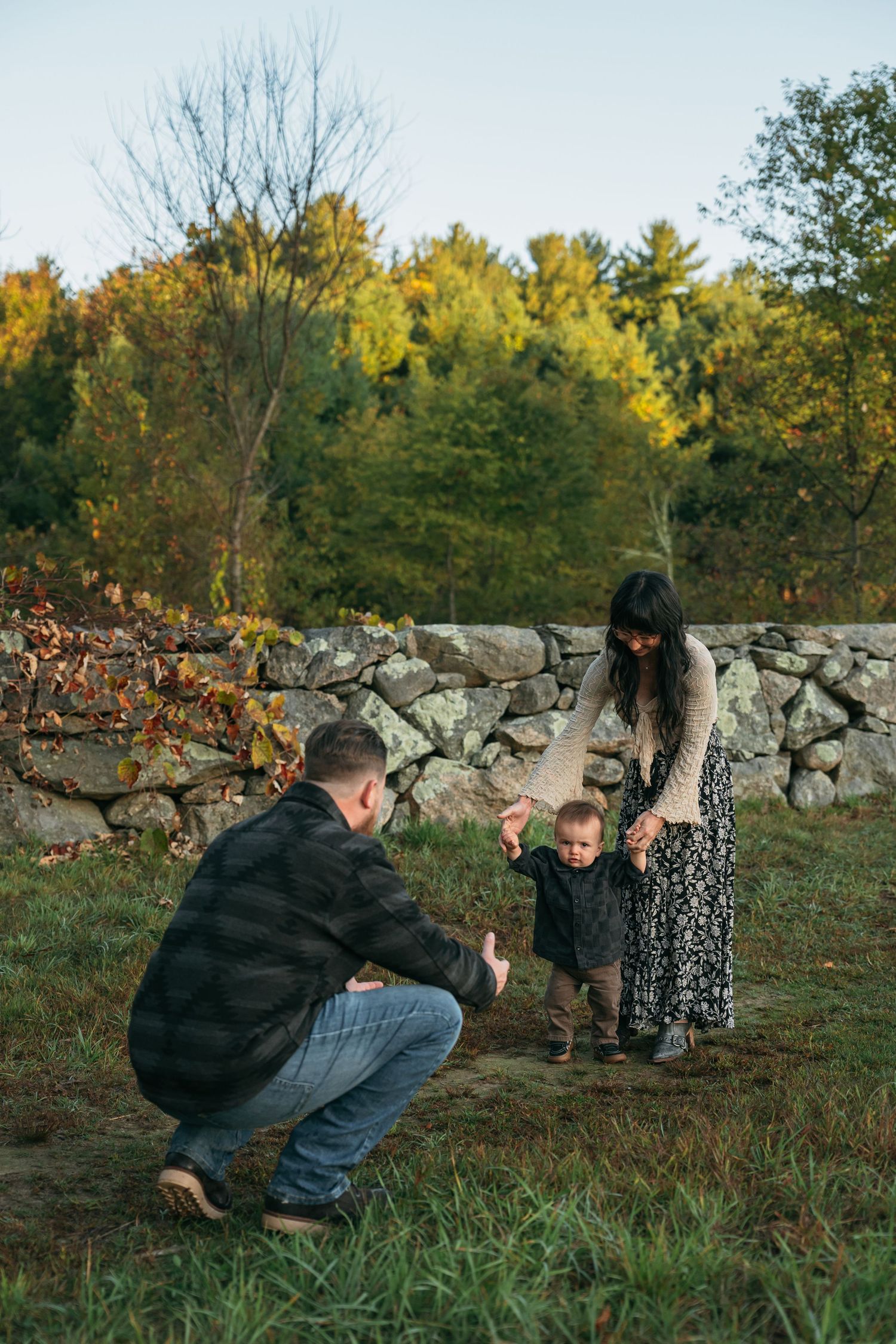 Playful outdoor photo session by a rustic stone wall during golden hour.