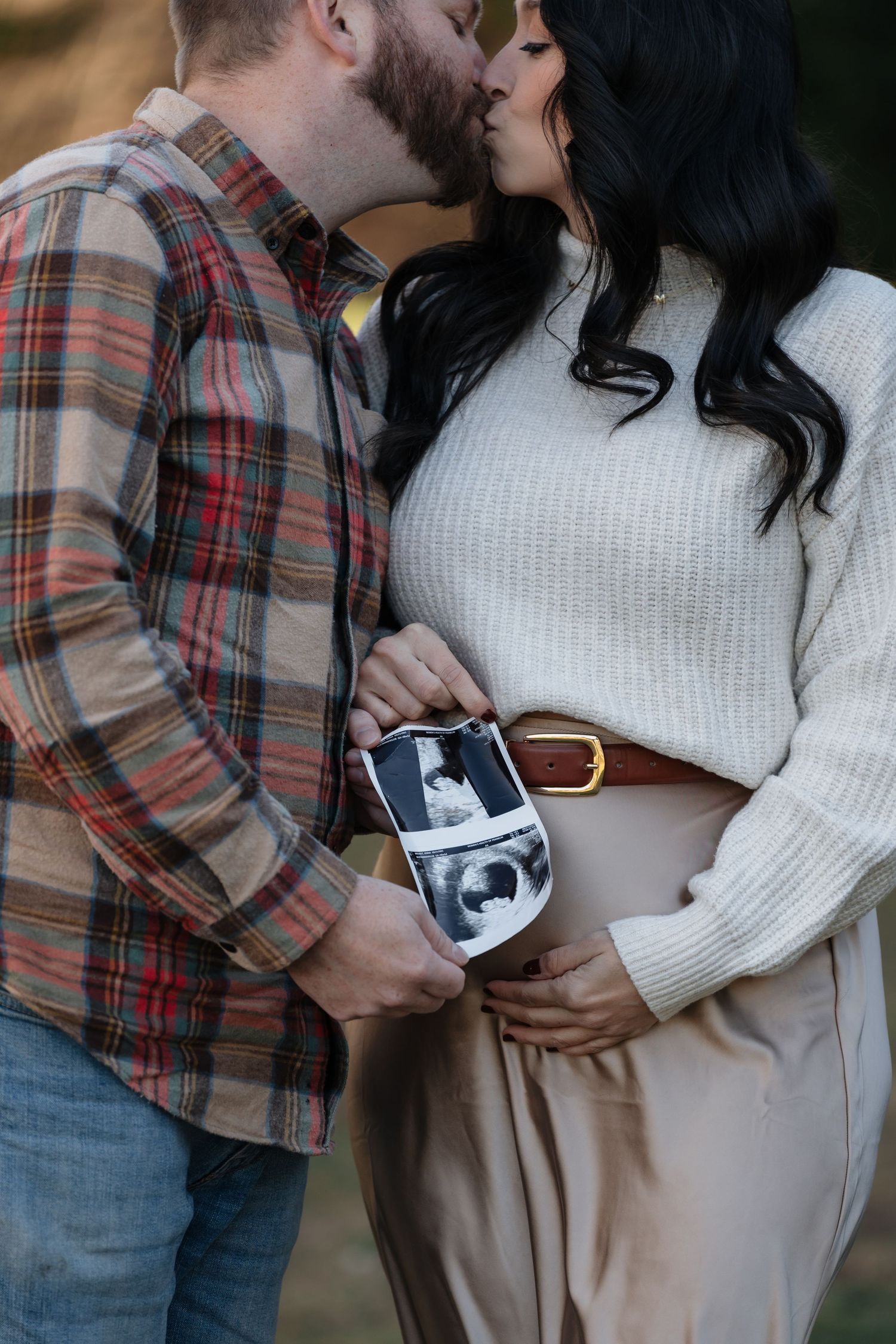 Couple holds ultrasound photos while sharing tender moments during maternity photoshoot.