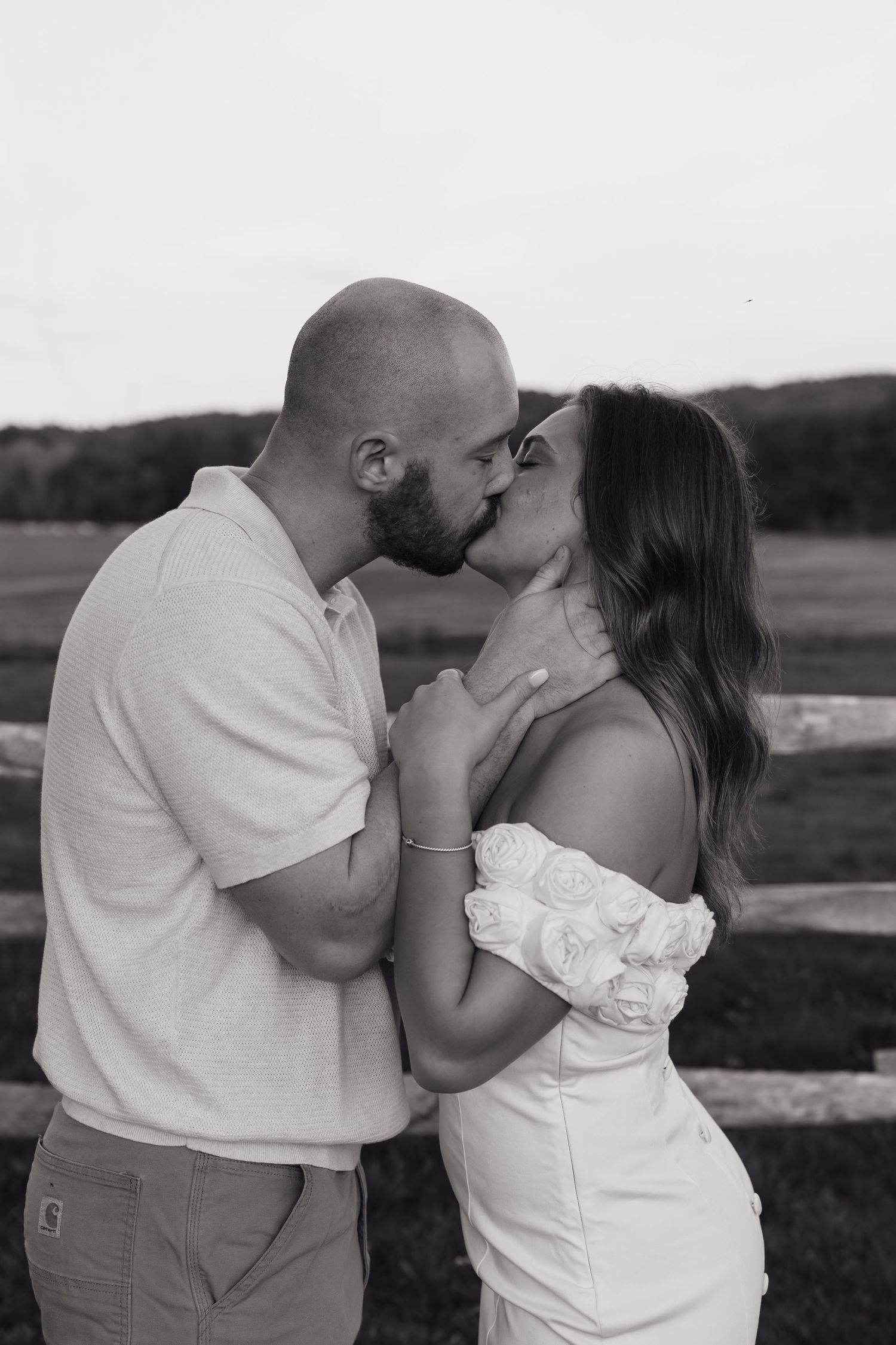An intimate black and white portrait of a couple sharing romantic moments by a fence.