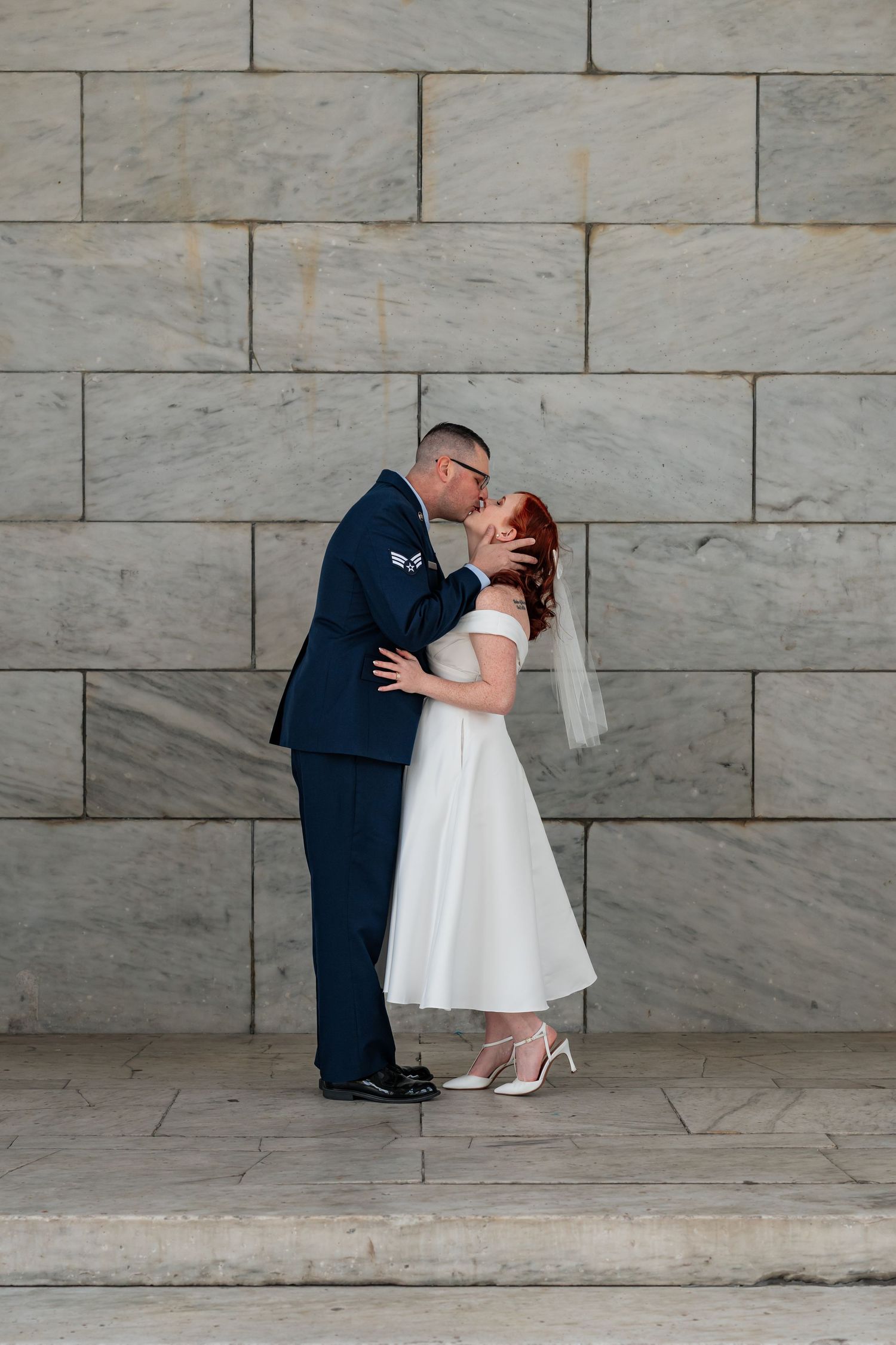 A romantic wedding moment against a marble wall backdrop.