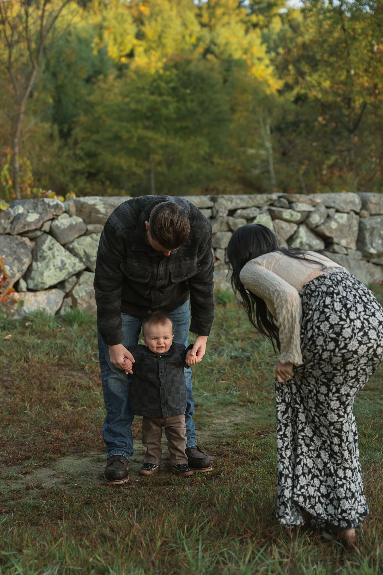 Family plays peek-a-boo game near stone wall during fall photo session.