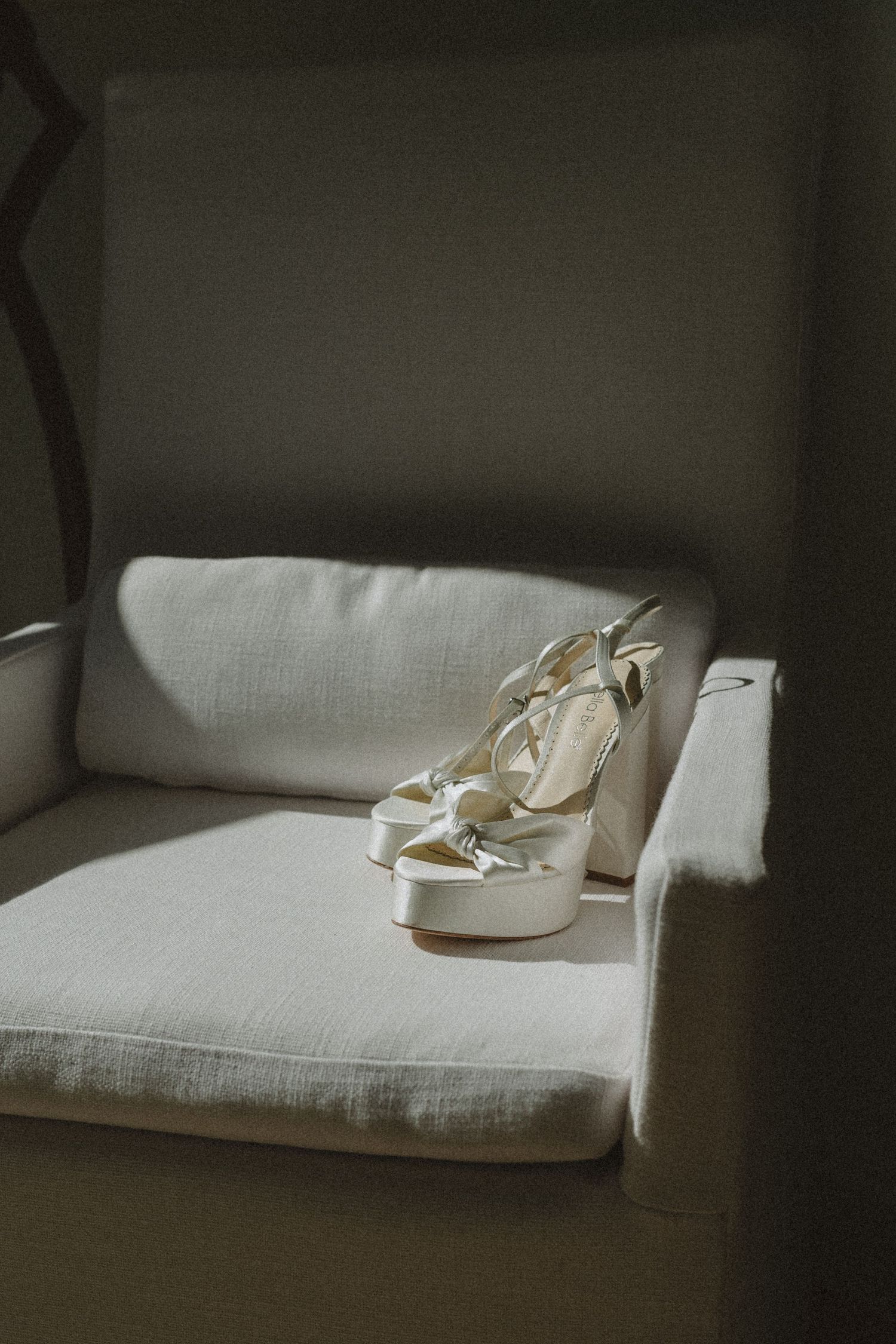 Elegant white platform wedding shoes placed on a light gray armchair in soft natural lighting.