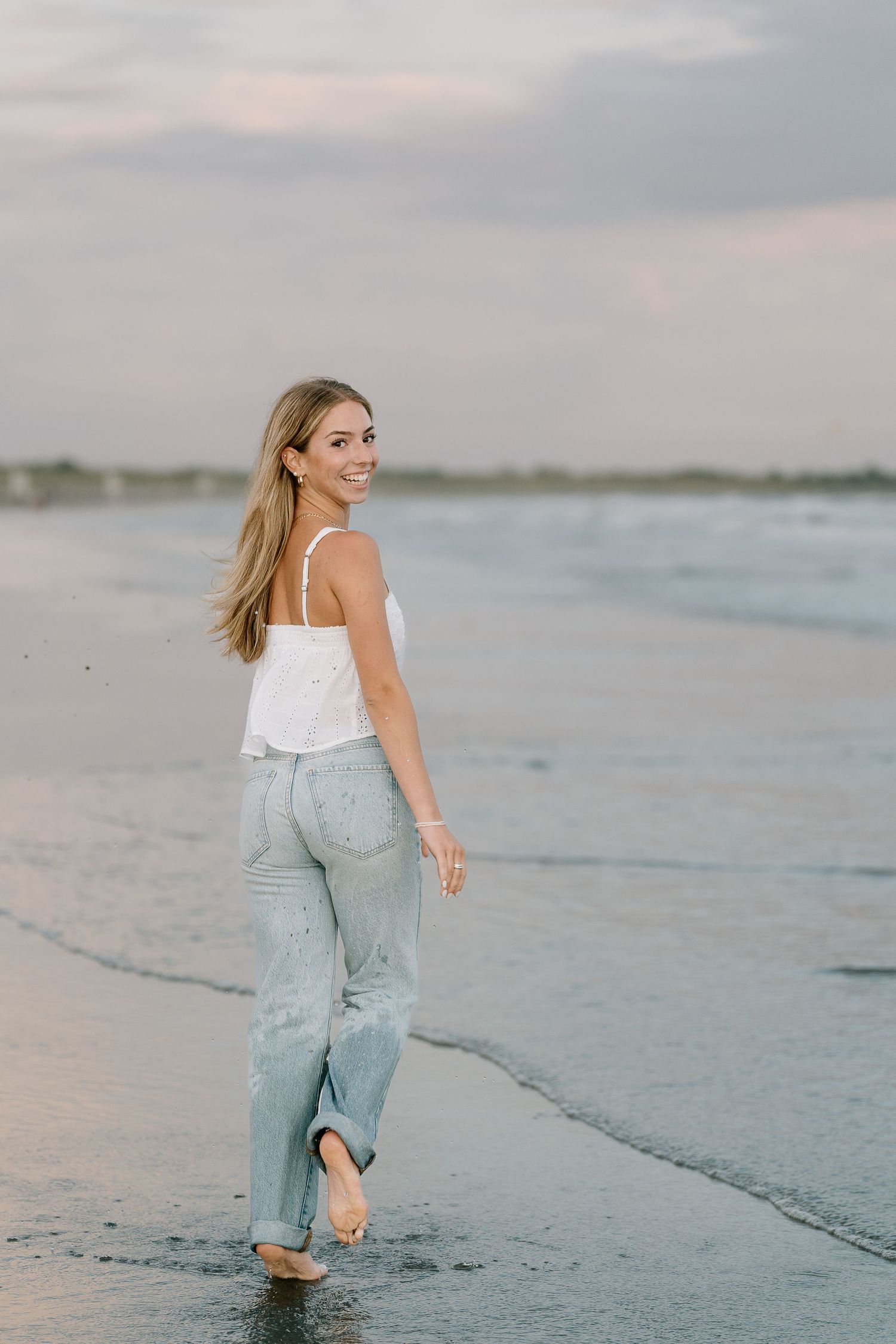 Playful beach photoshoot with distressed denim and white top.