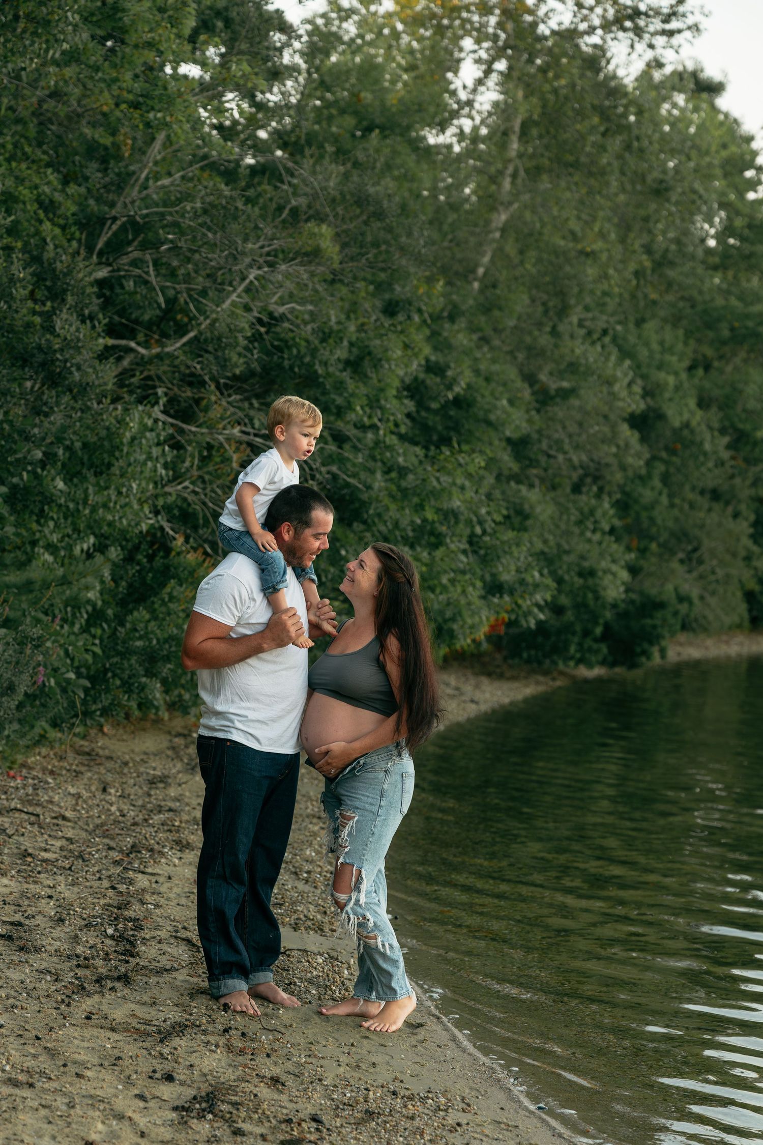Couple embracing on riverbank during outdoor photoshoot.