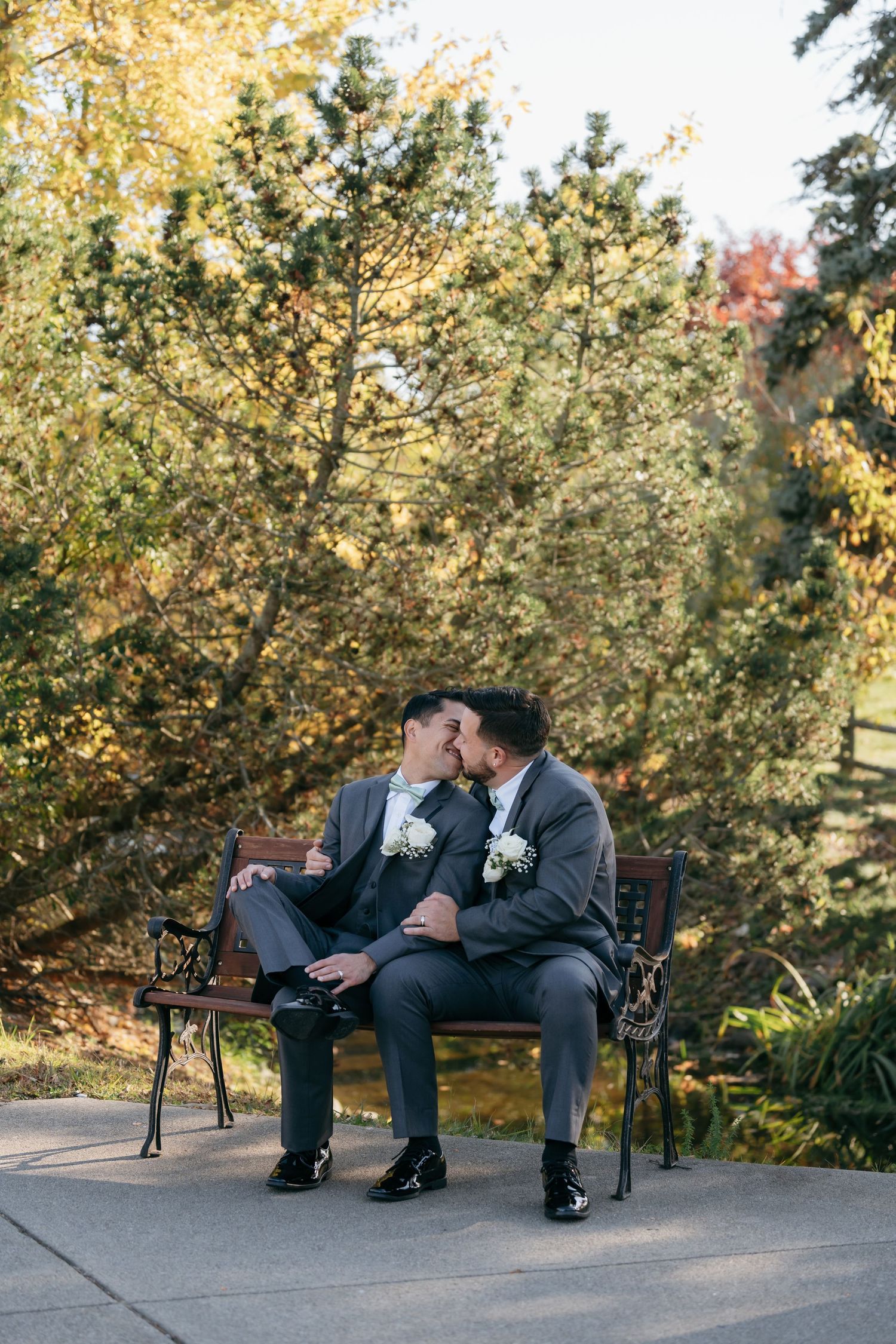 A romantic moment between newlyweds sitting on a garden bench surrounded by autumn foliage.
